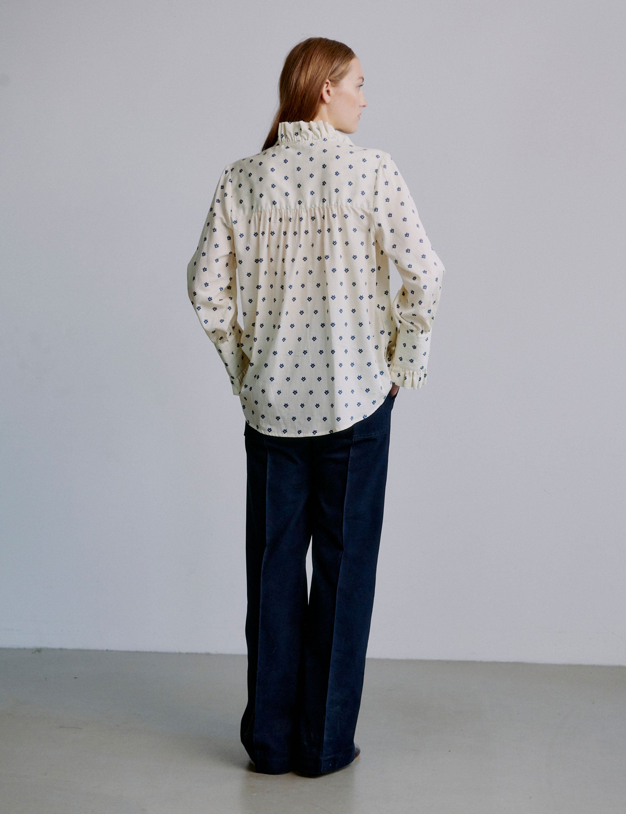 Woman wearing a polka dot blouse and dark blue wide pants against a plain background