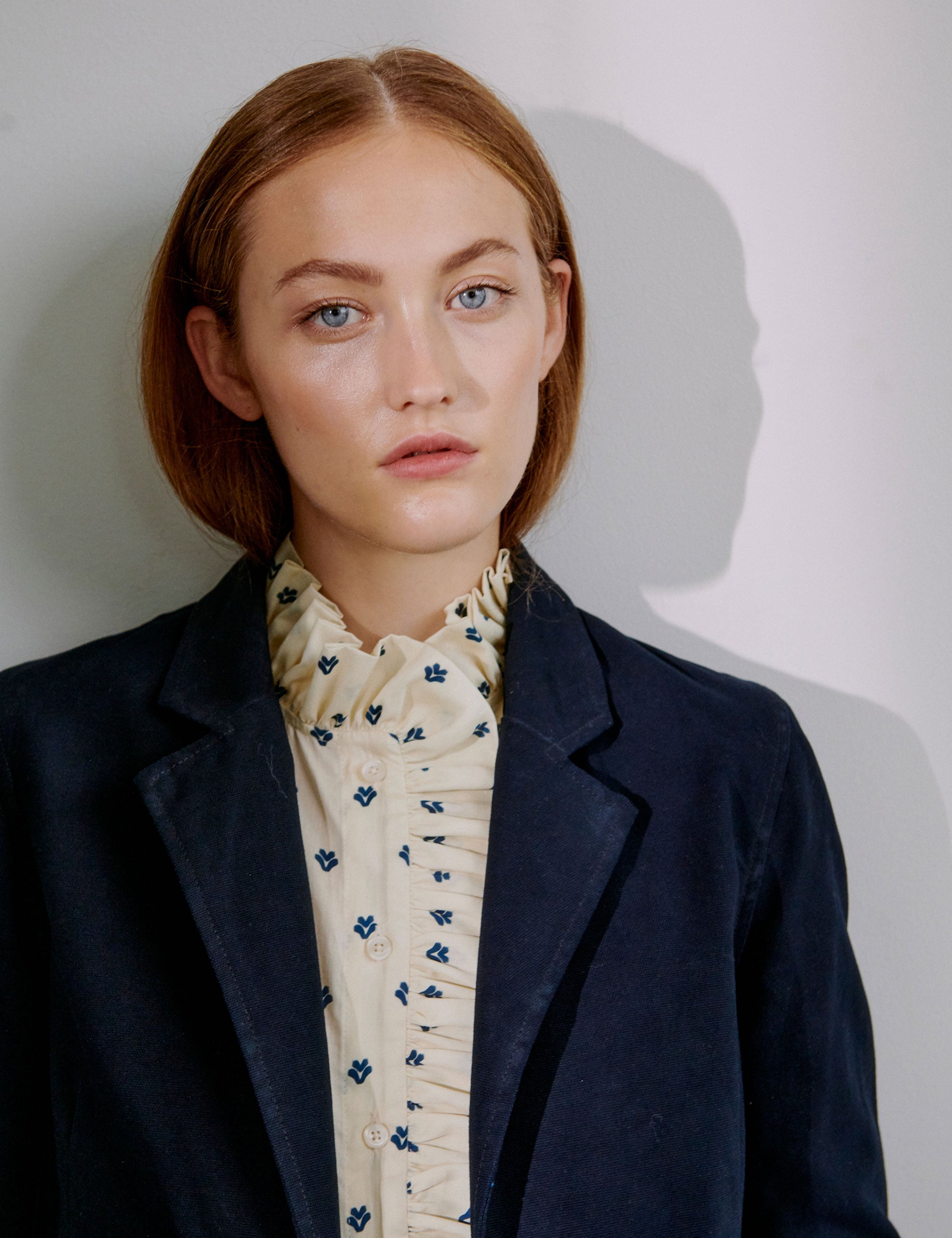 Woman wearing a dark blue blazer over a cream blouse with floral details