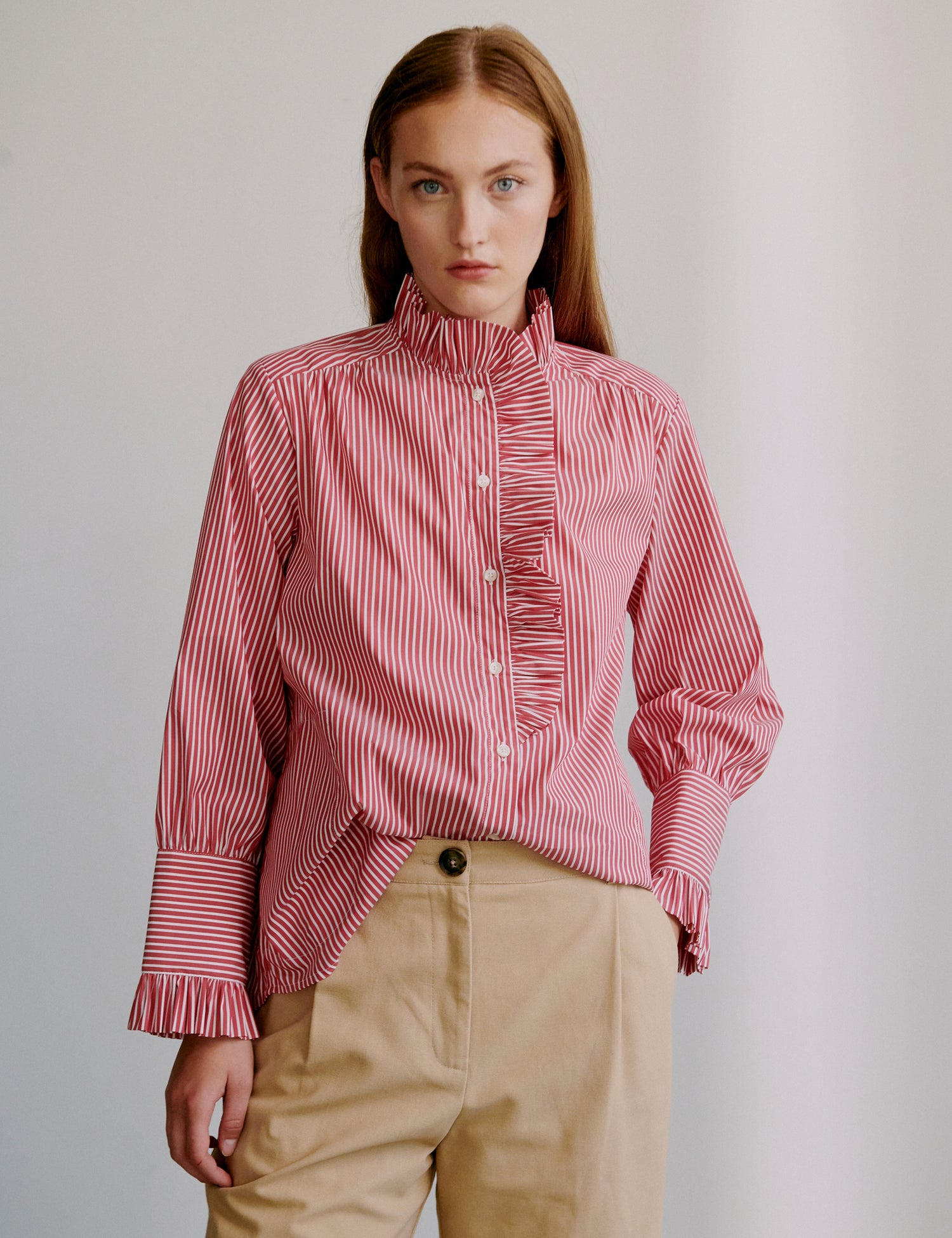 Woman wearing a pink striped frill shirt and beige shorts against a plain background