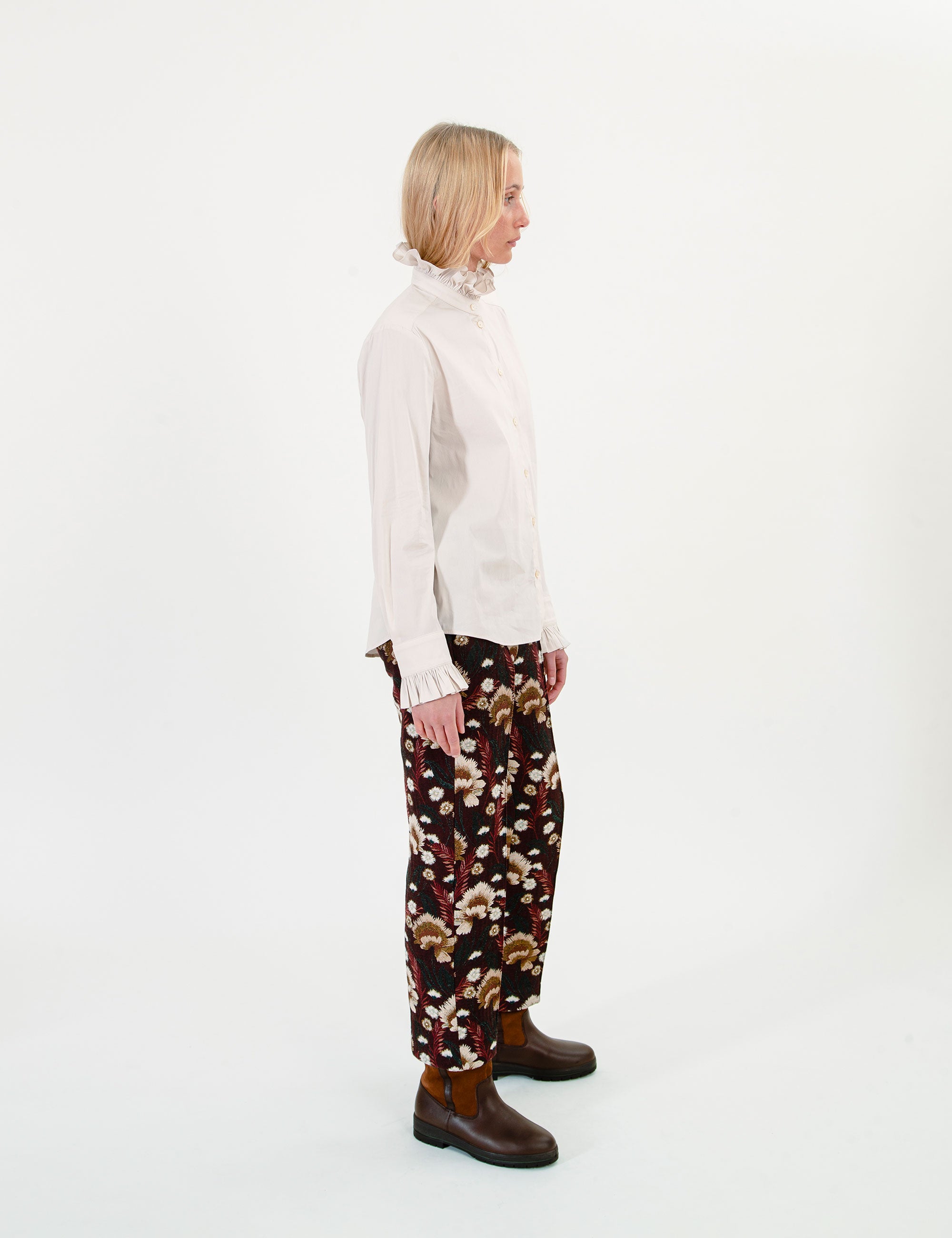 Woman wearing a cream blouse and brown patterned pants on a white background
