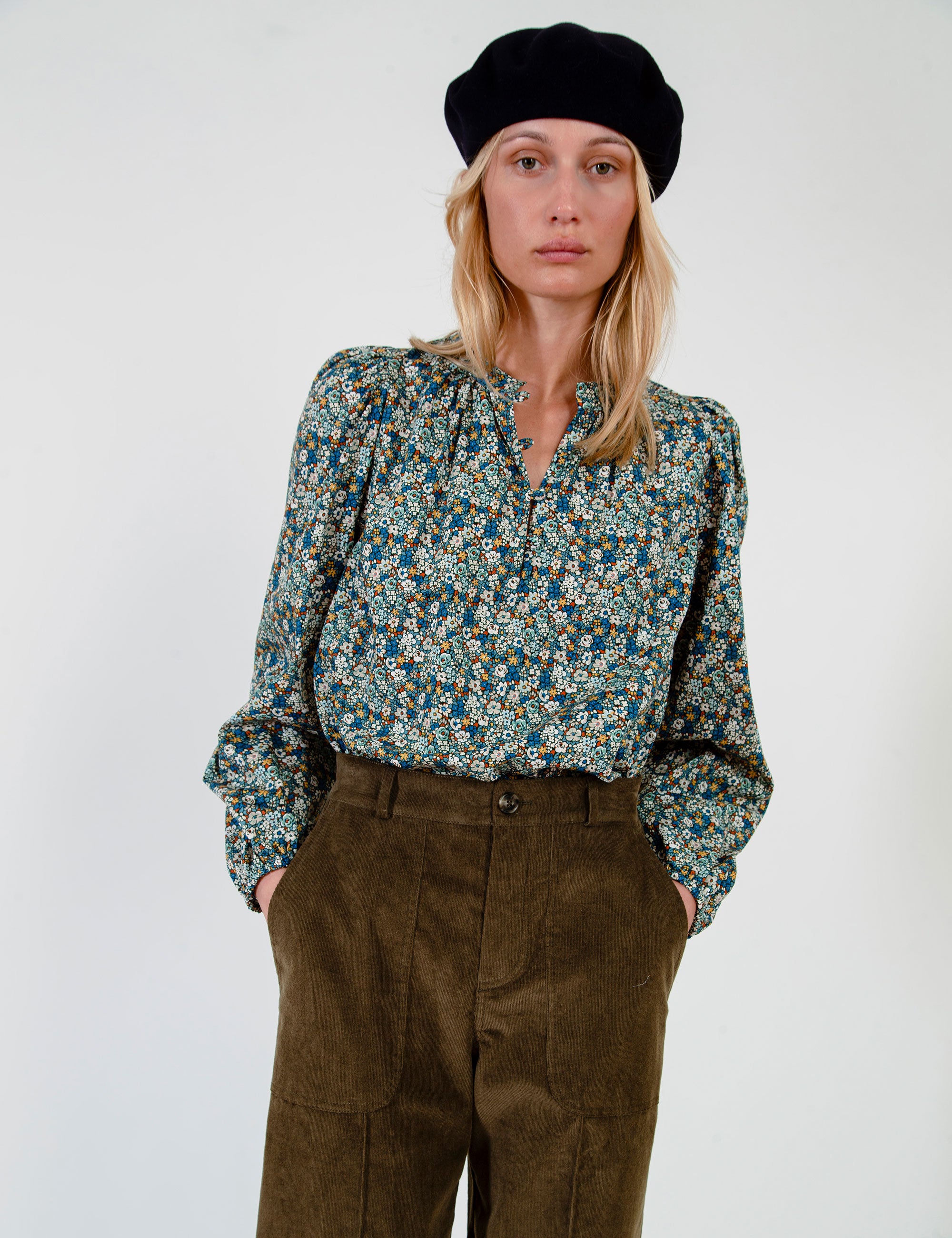 Woman wearing a patterned blouse and olive green pants on a white background