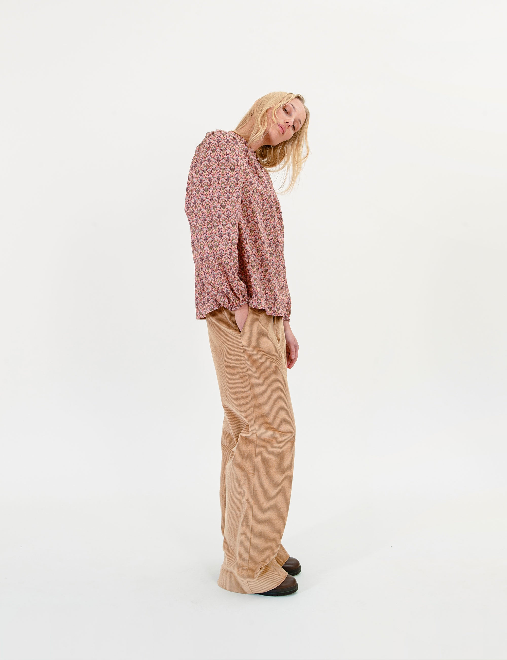 Woman wearing a floral blouse and beige pants on a white background