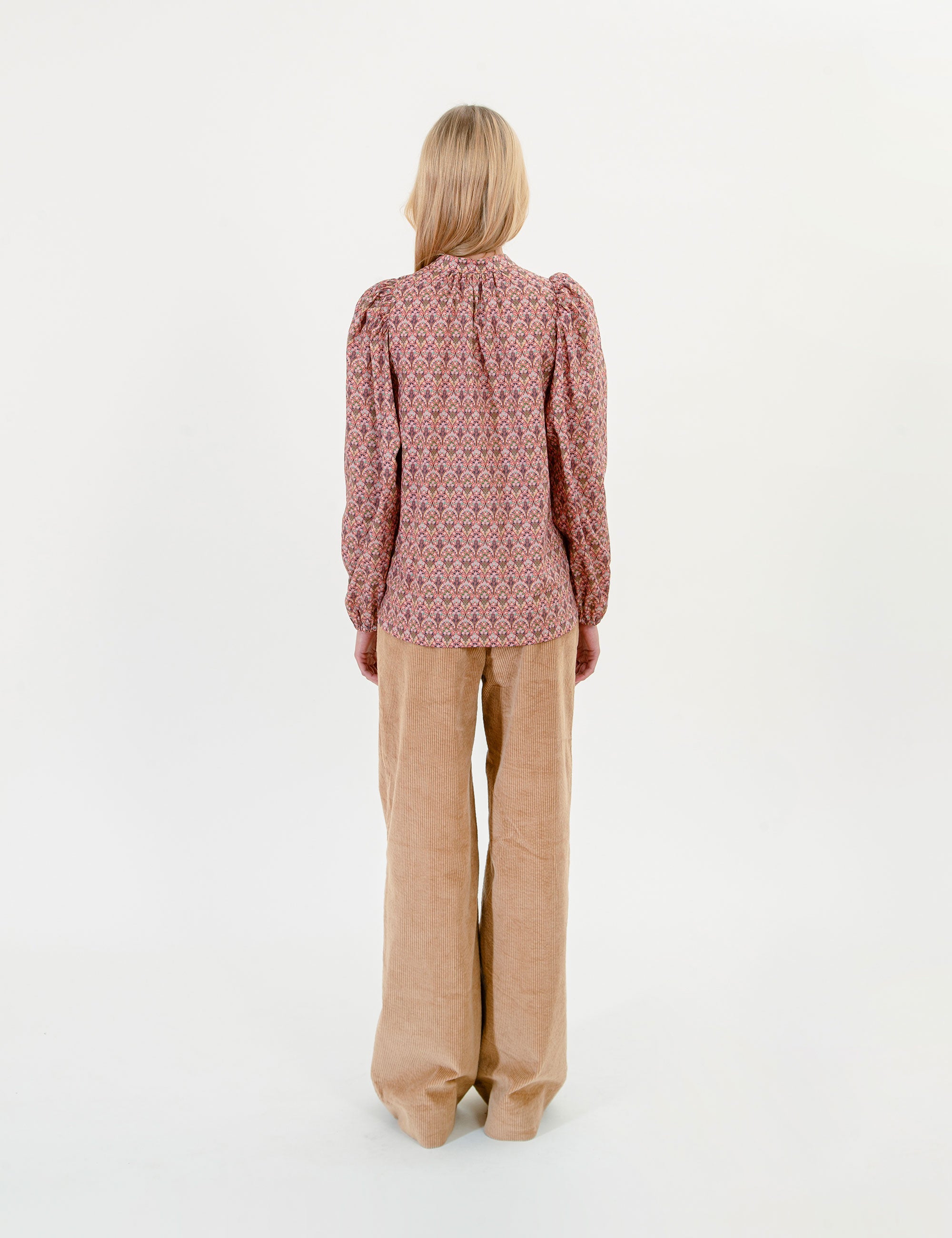 Woman wearing a patterned blouse and beige pants on a white background