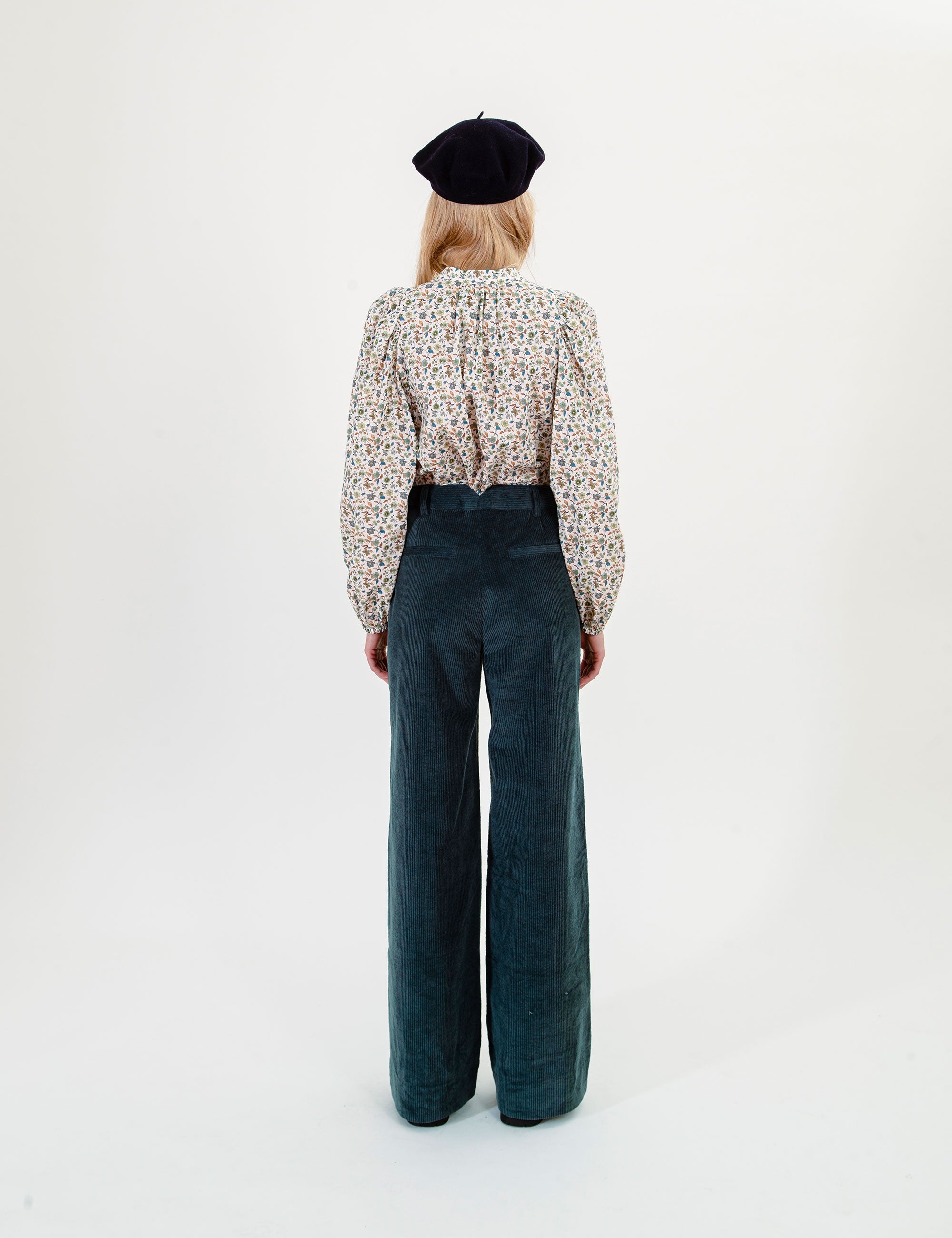 Woman wearing a patterned blouse and dark corduroy pants on a white background