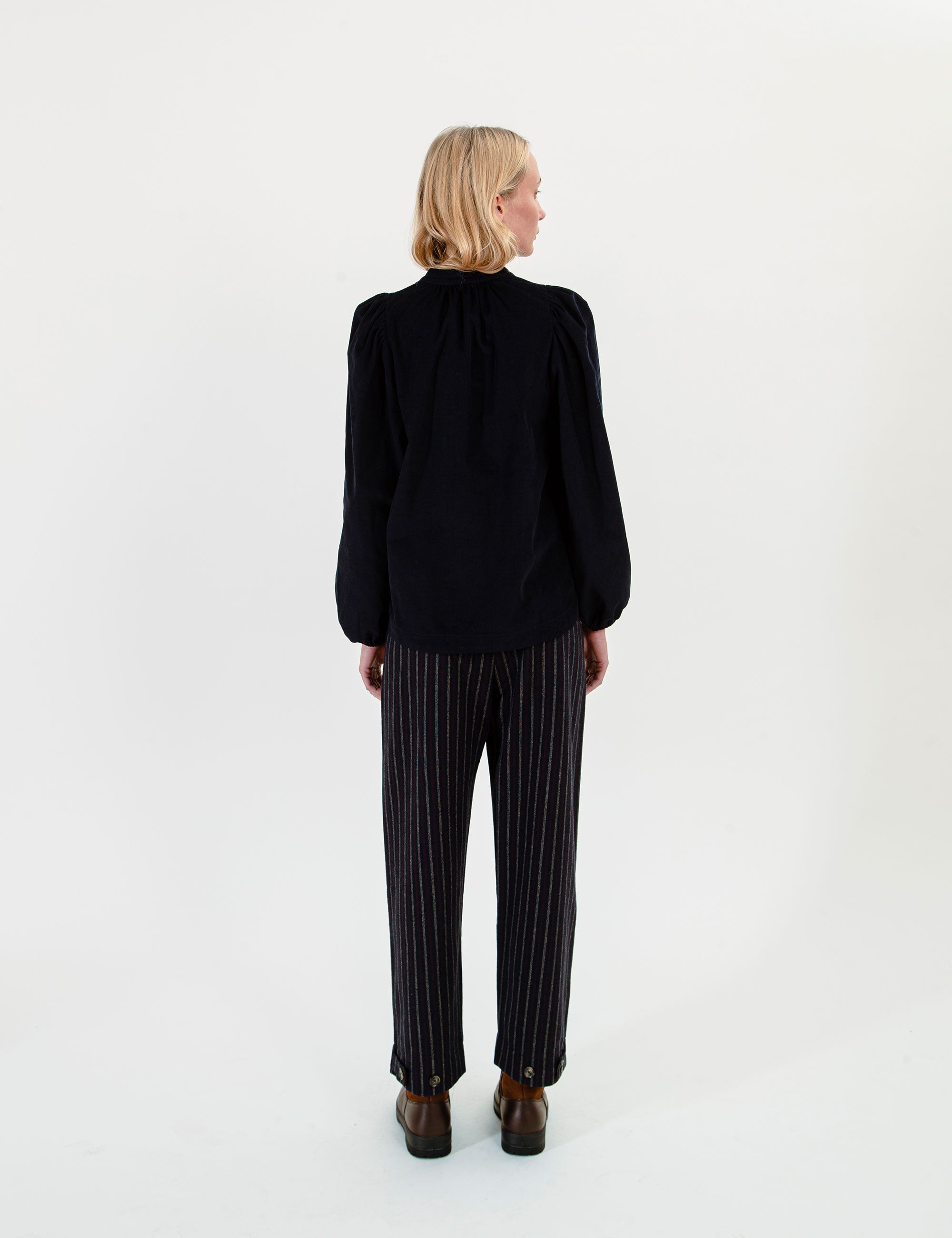Woman wearing a dark blue corduroy blouse and striped pants on a white background