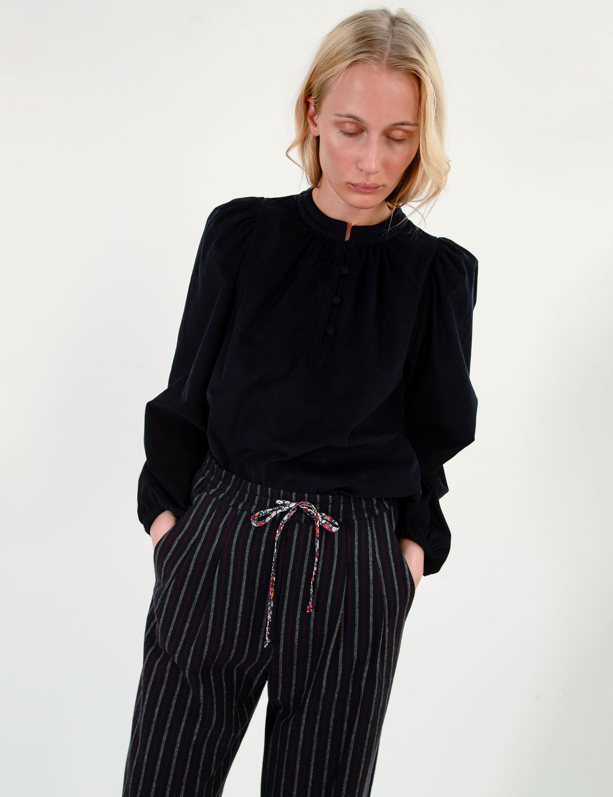 Woman wearing a dark blouse and striped pants against a white background