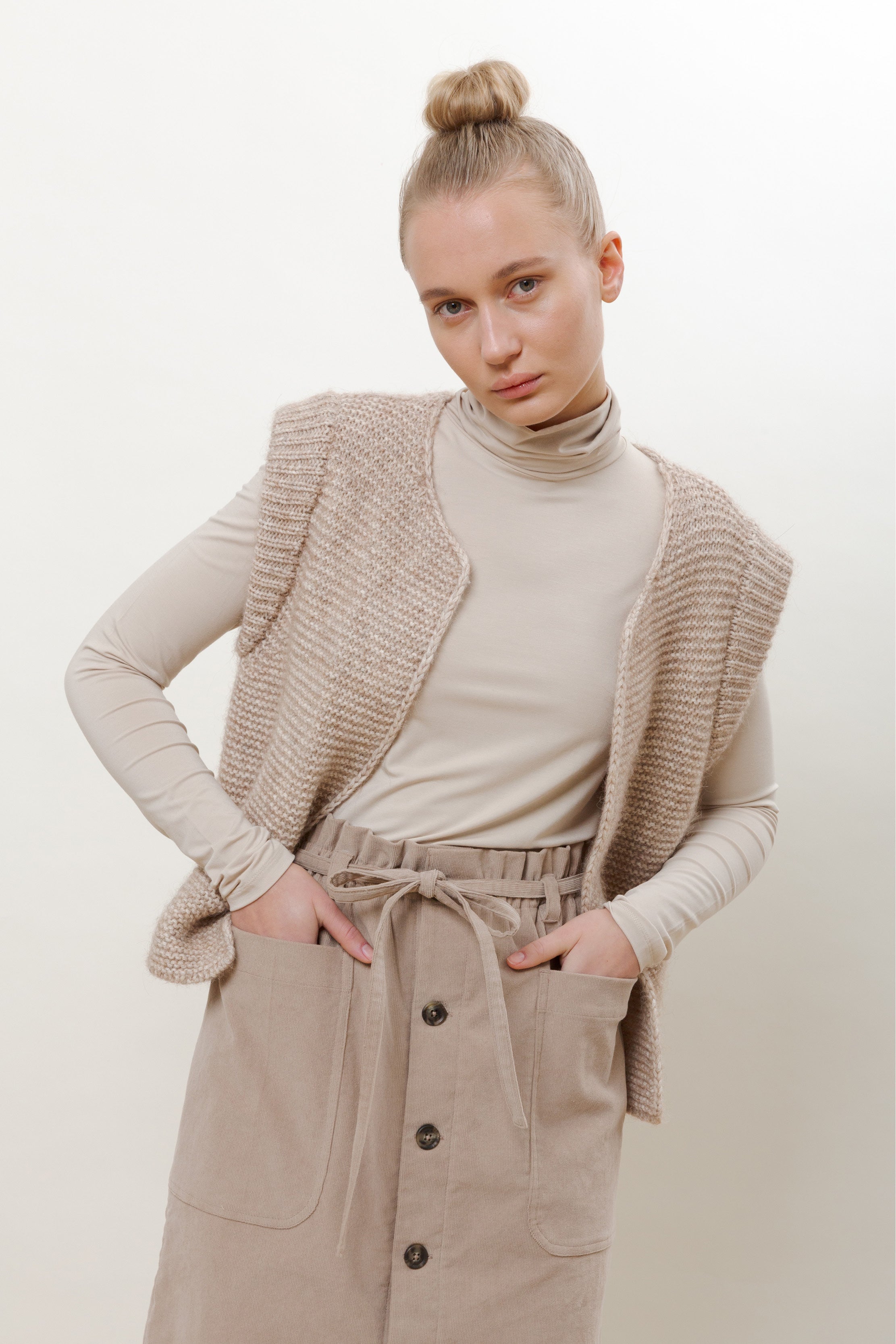 Woman in beige roll neck, beige knitted wool vest and beige corduroy skirt with pockets and buttons