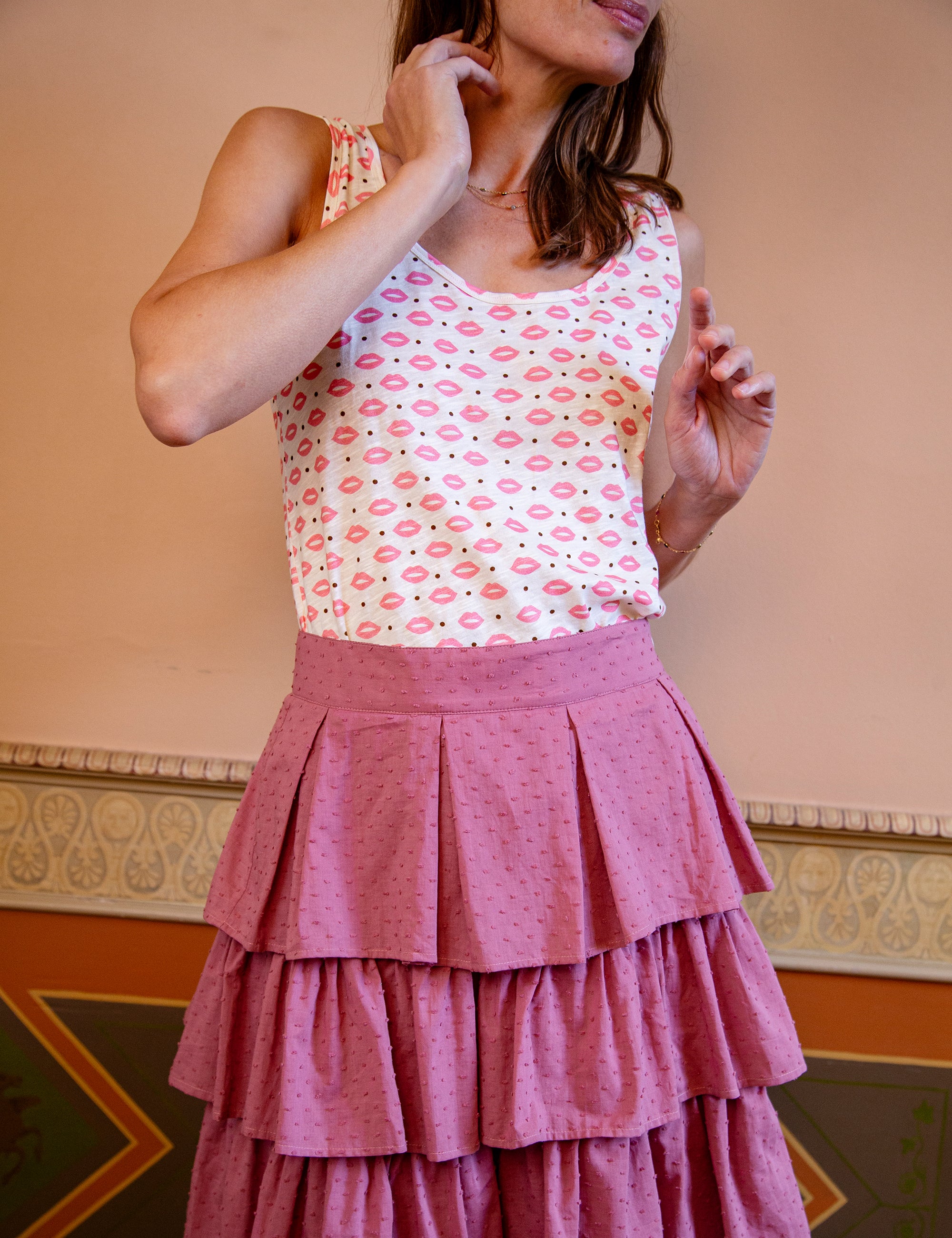 Woman wearing a sleeveless top with lip print and a pink tiered skirt against a beige wall.