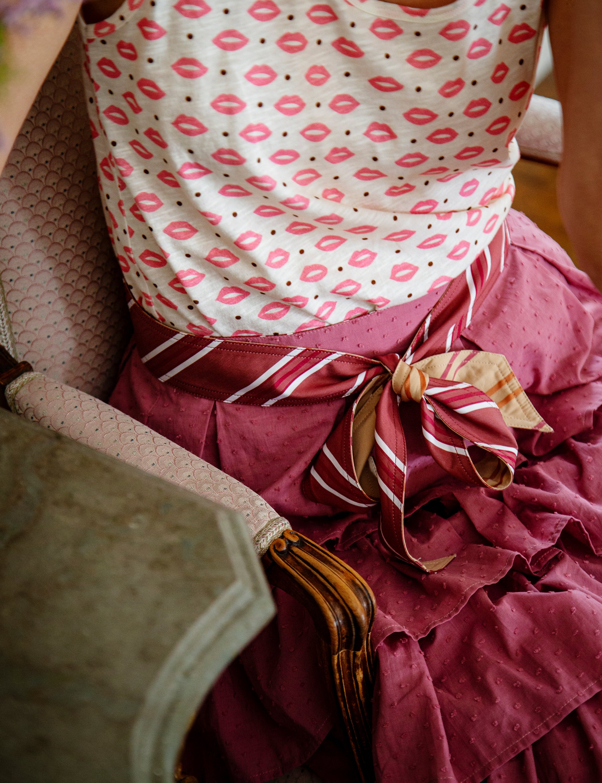 Woman wearing a top with pink lip patterns and a layered skirt sitting on a chair.