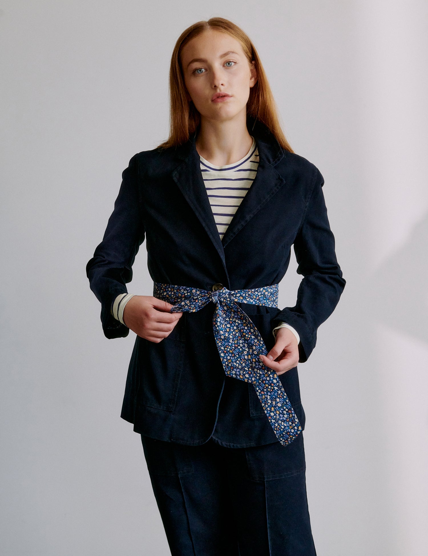 Woman wearing a navy blazer with a patterned fabric belt against a plain background