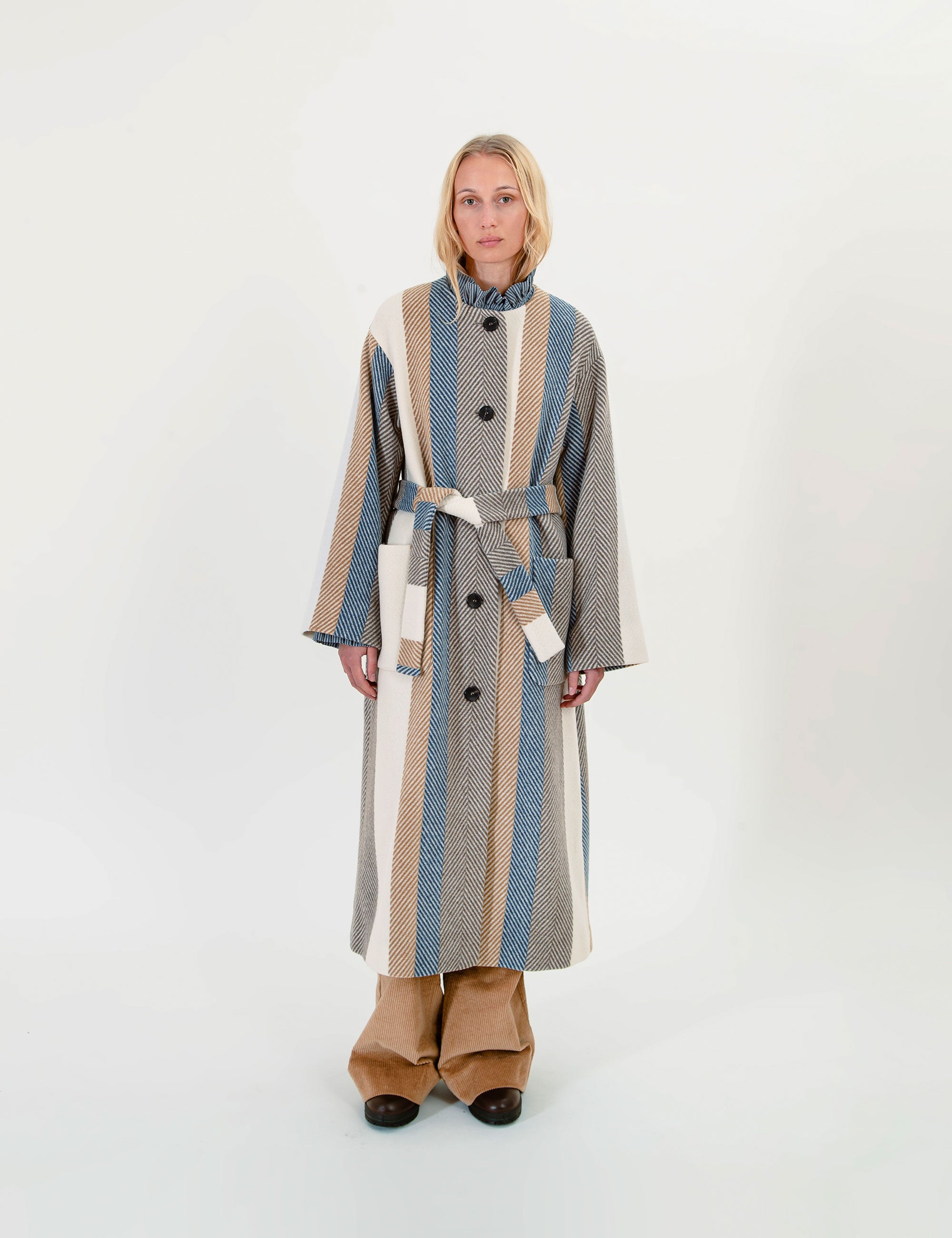 Woman wearing a long, striped wool coat with a belt on a white background