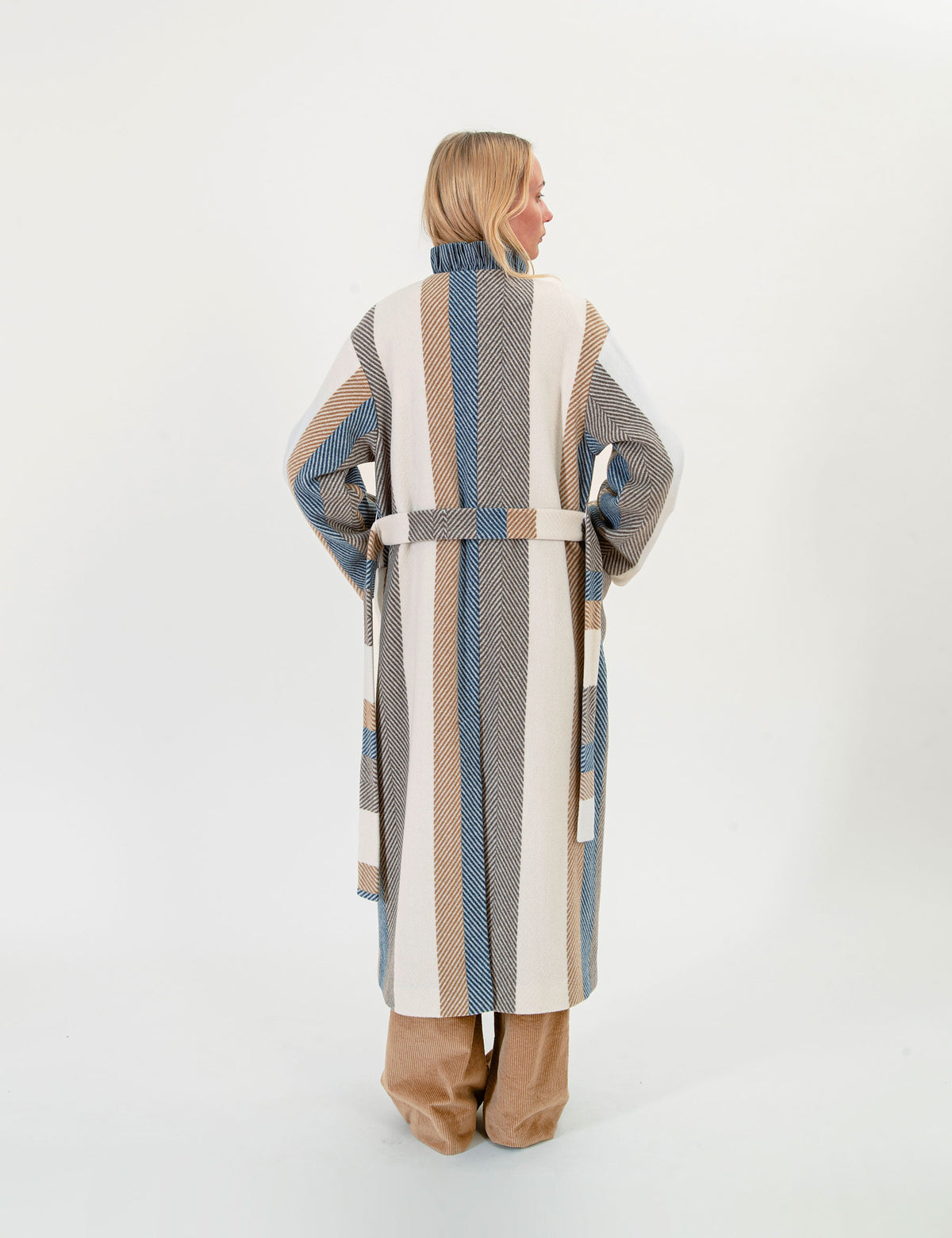 Woman wearing a long, striped wool coat with a belt on a white background