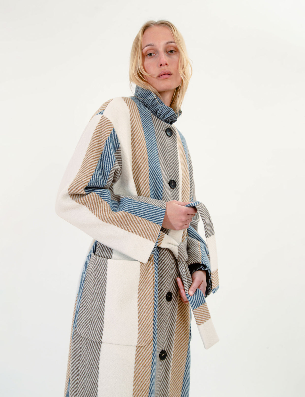 Woman wearing a long, striped wool coat with a belt on a white background