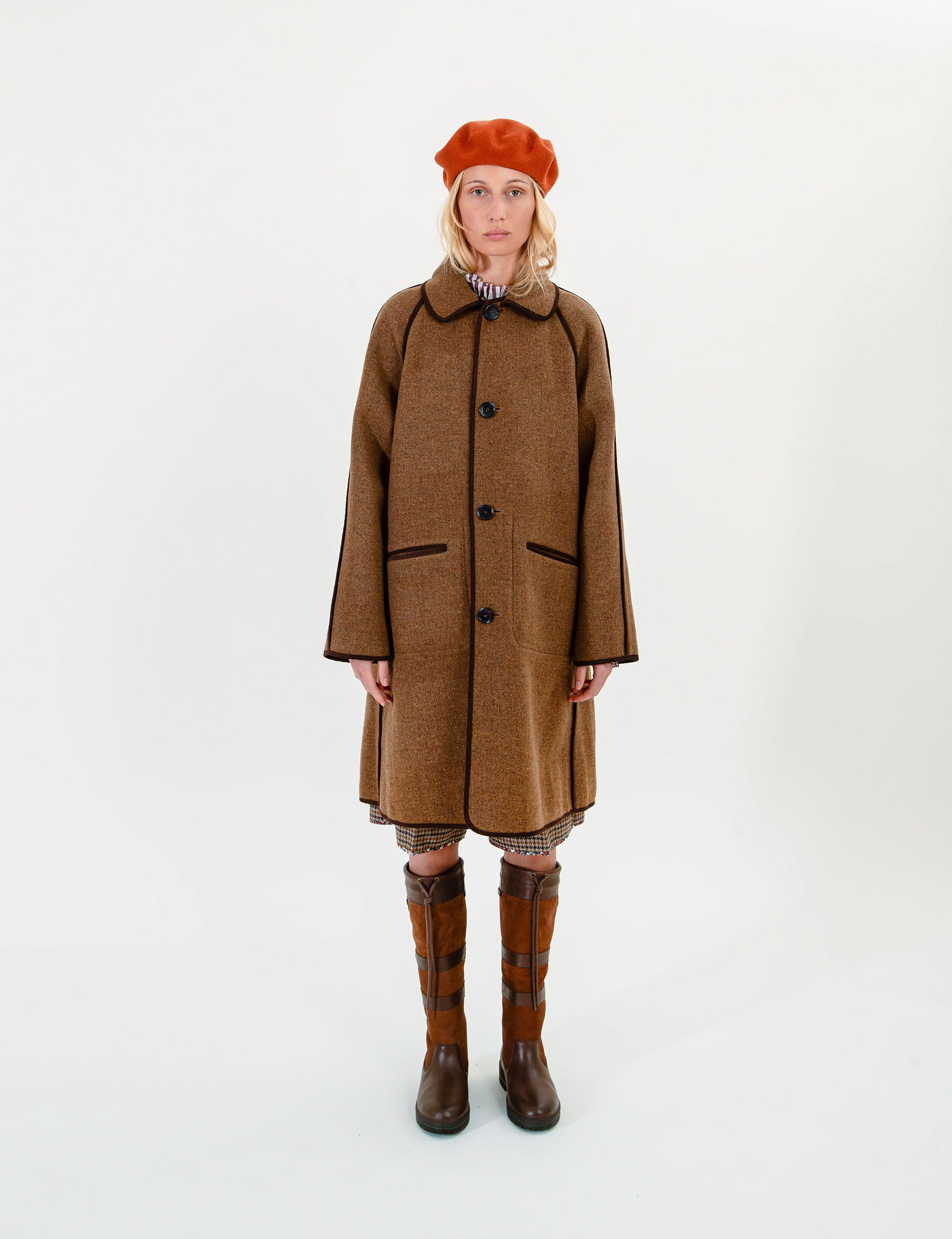 Woman wearing a brown coat, red beret, and brown boots on a white background