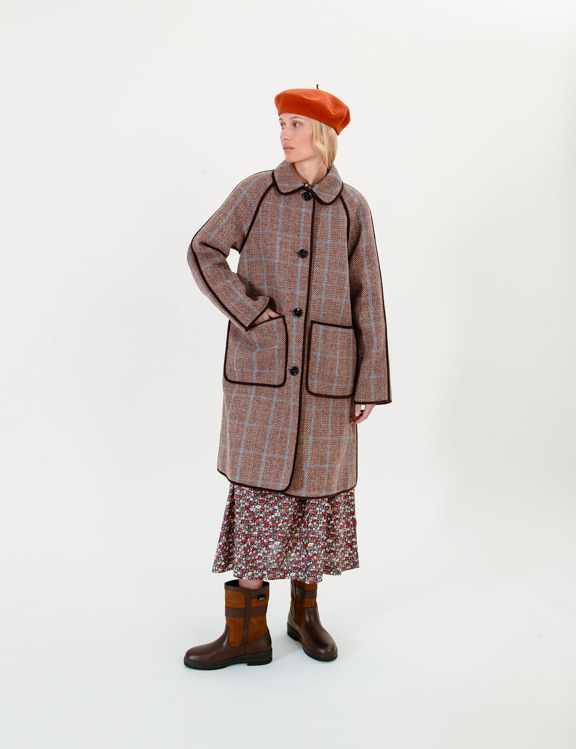 Woman wearing a plaid coat, floral skirt, and brown boots on a white background