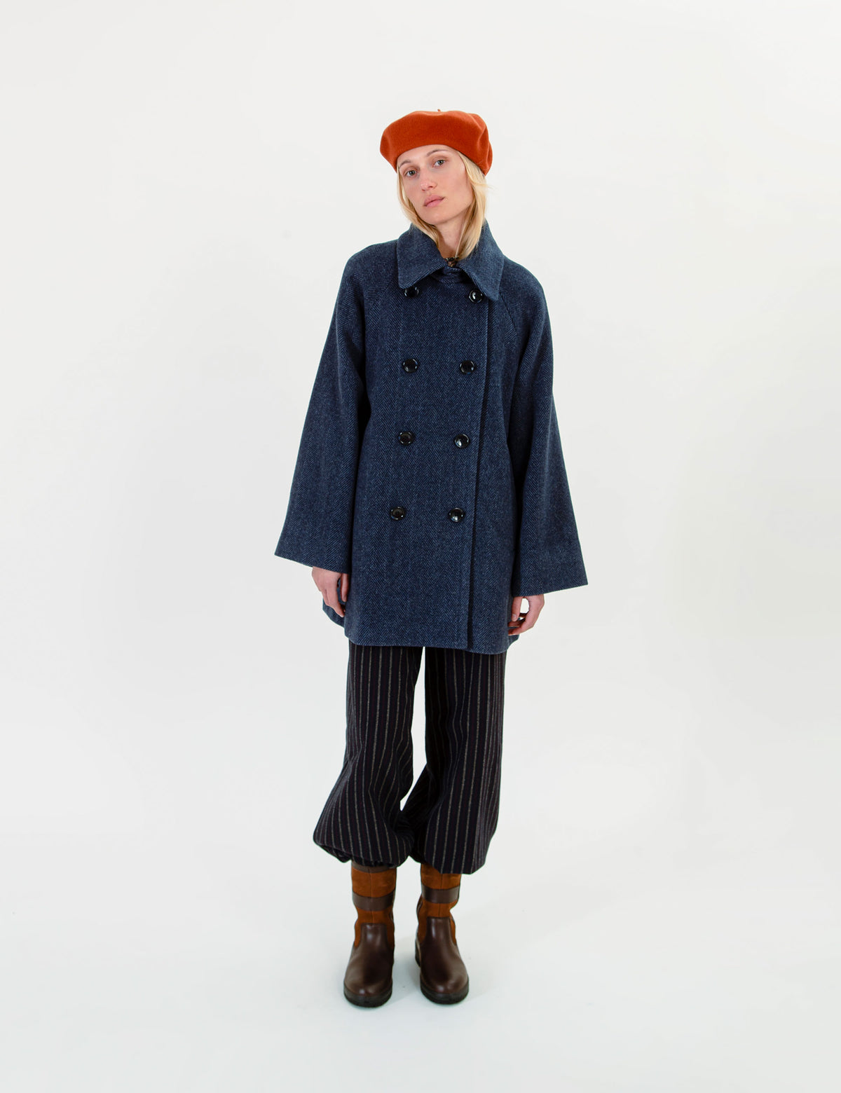 Woman  wearing a blue wool jacket, striped pants, and a red beret on a white background
