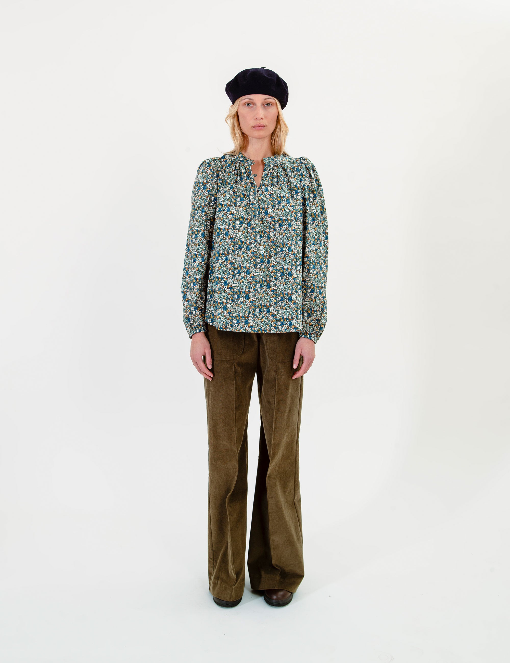 Woman wearing a patterned blouse and olive green pants on a white background