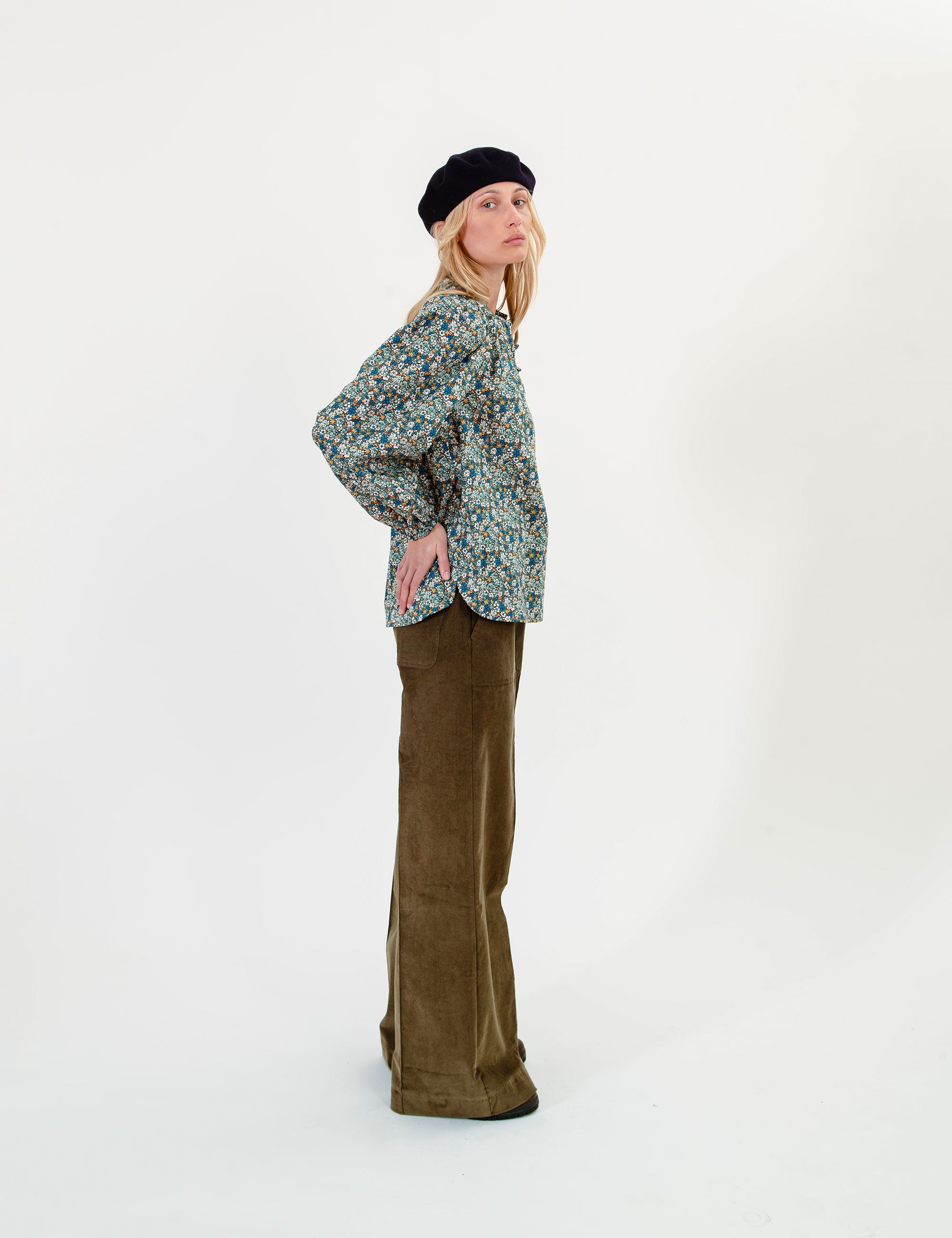 Woman wearing a floral blouse, olive green pants and a dark beret