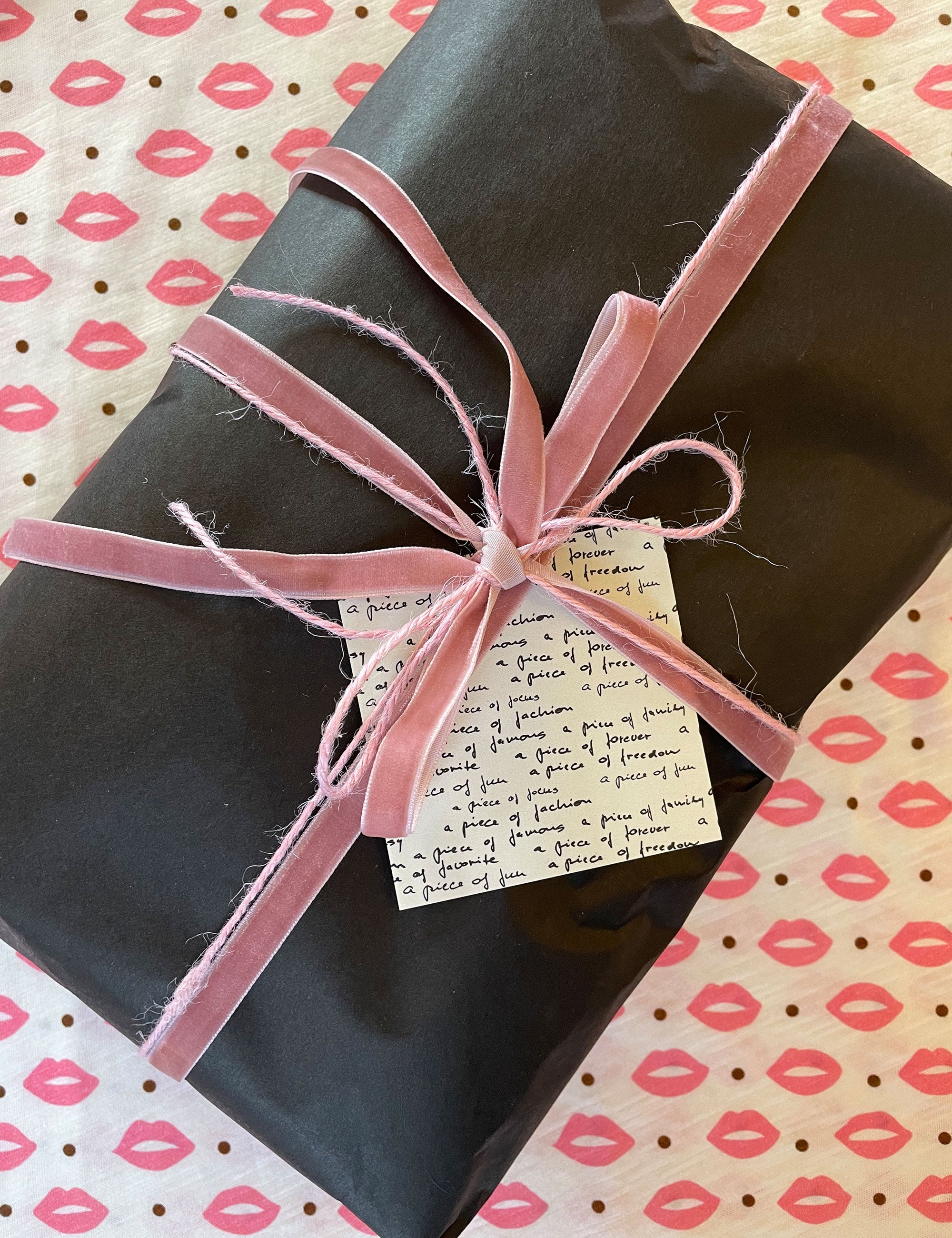 Christmas gift in black wrapping, pink ribbon and greeting card lying on a t-shirt with pink kisses