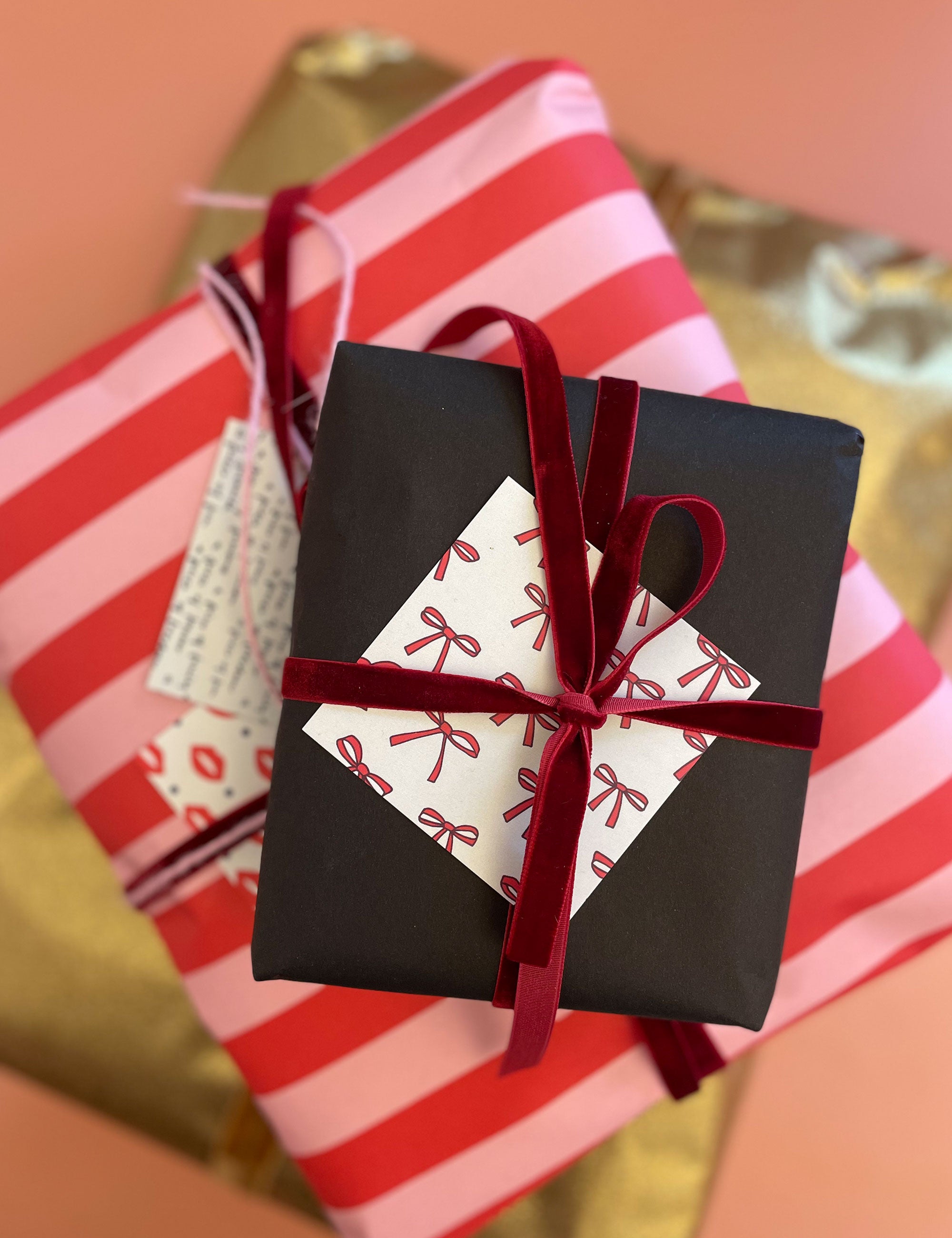 Two Christmas gifts in red and pink wrapping with red ribbon and black wrapping with red ribbon