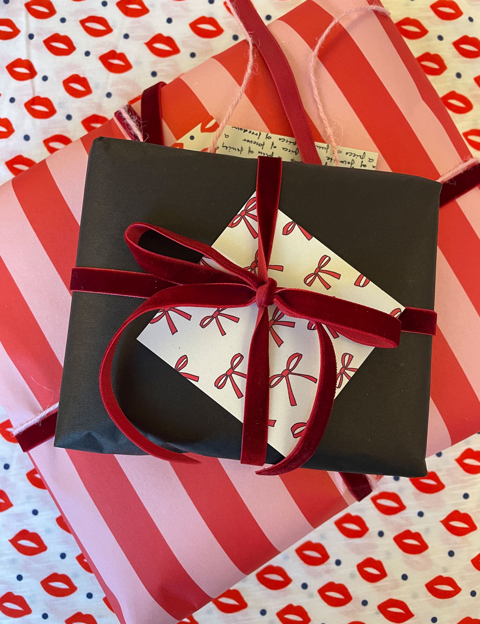 Two Christmas gifts in red and pink wrapping with red ribbon and black wrapping with red ribbon