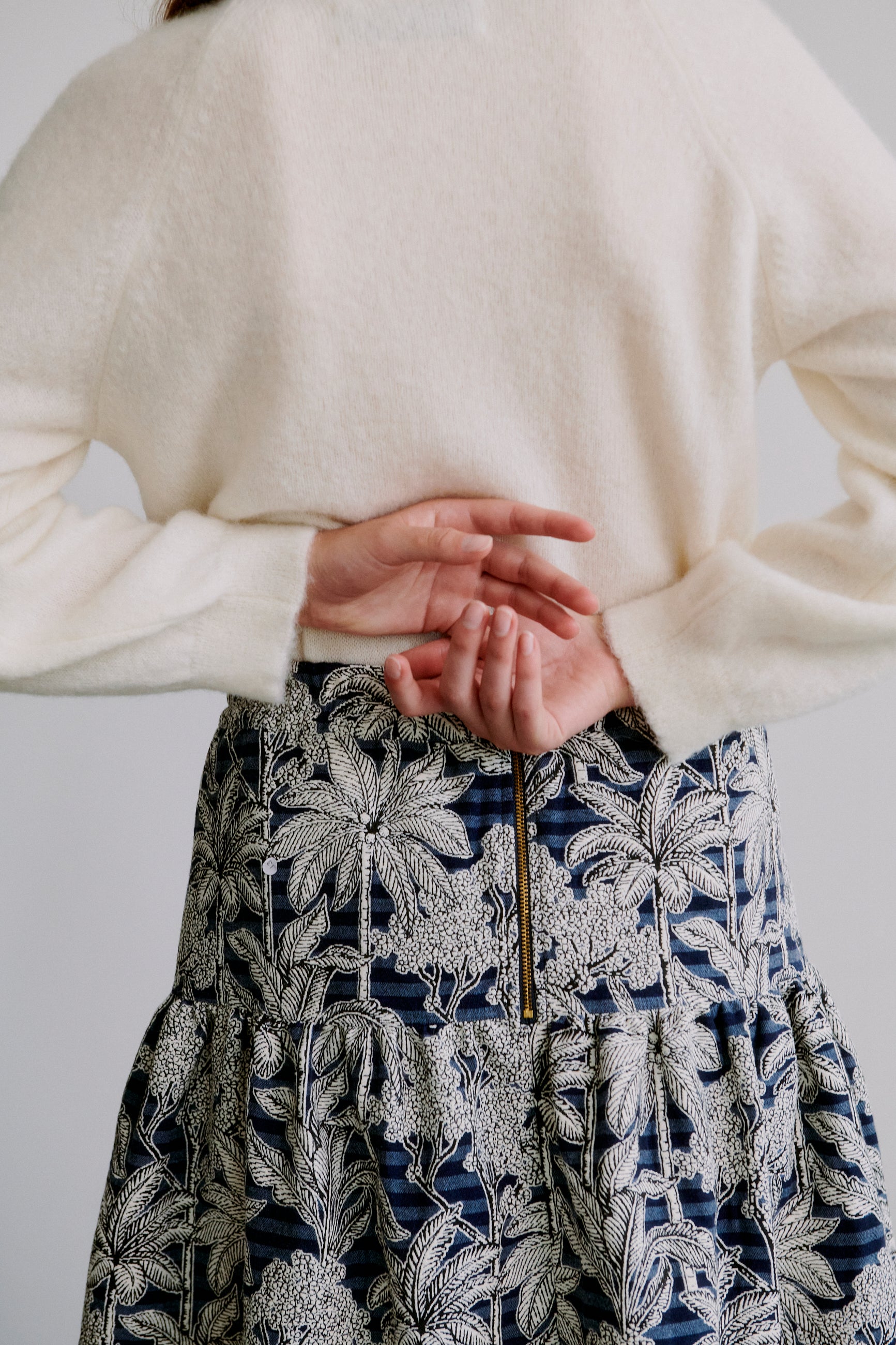 Woman wearing a cream knit sweater and a blue floral patterned skirt with zipper on the back