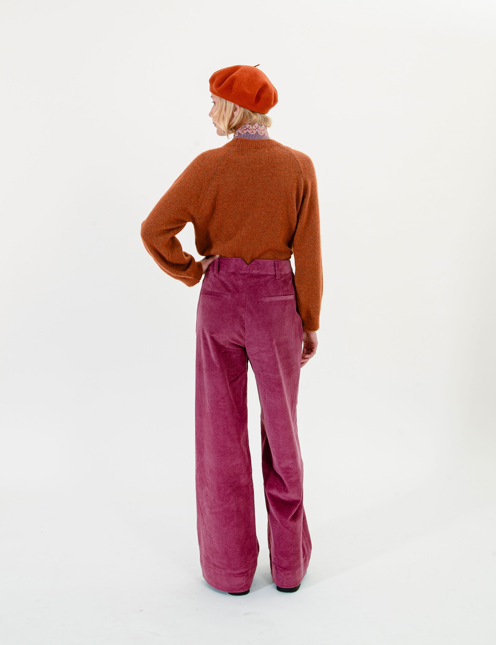 Woman wearing a brown sweater, red beret, and pink pants on a white background