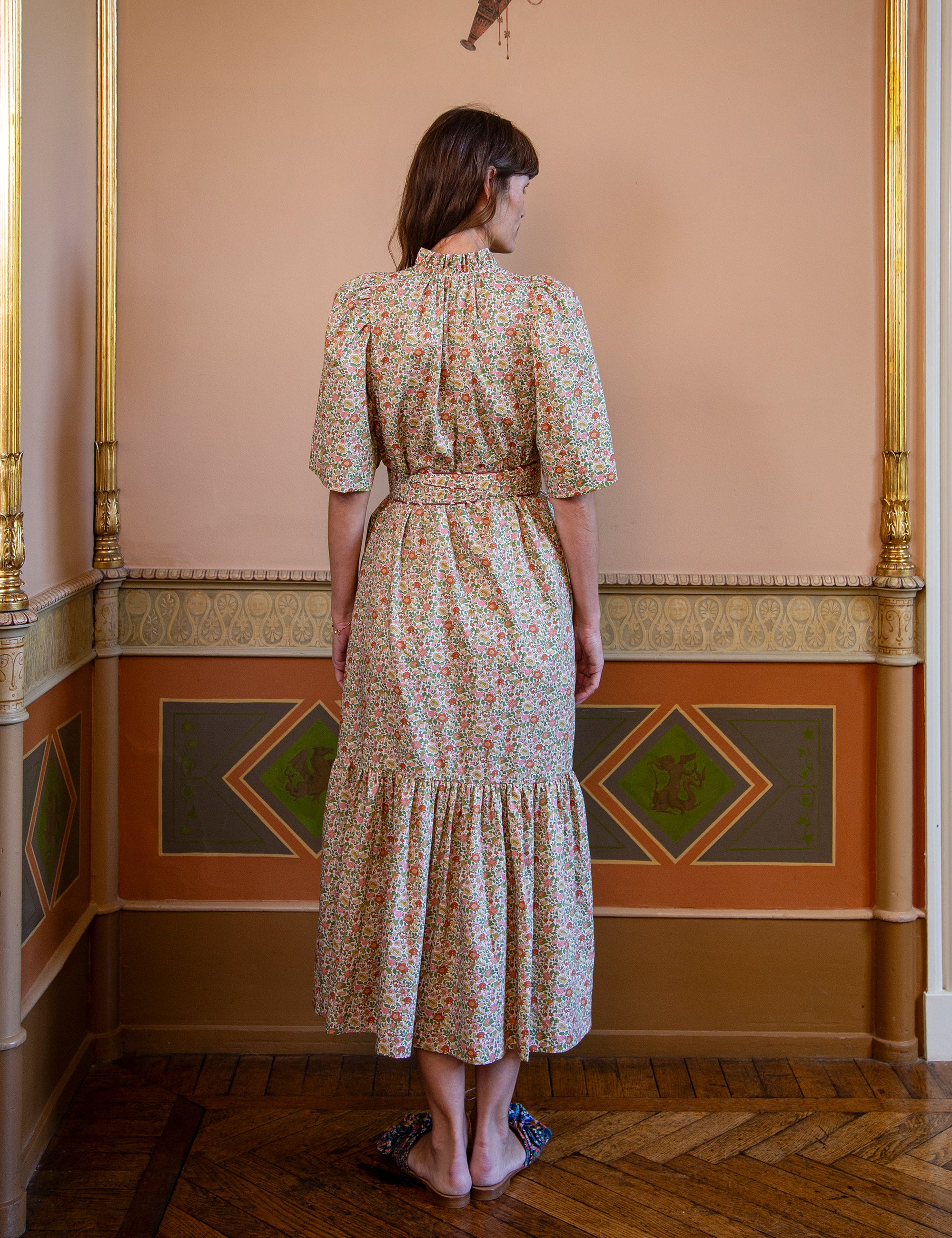 Woman wearing a floral dress standing in an ornate room with decorative walls.