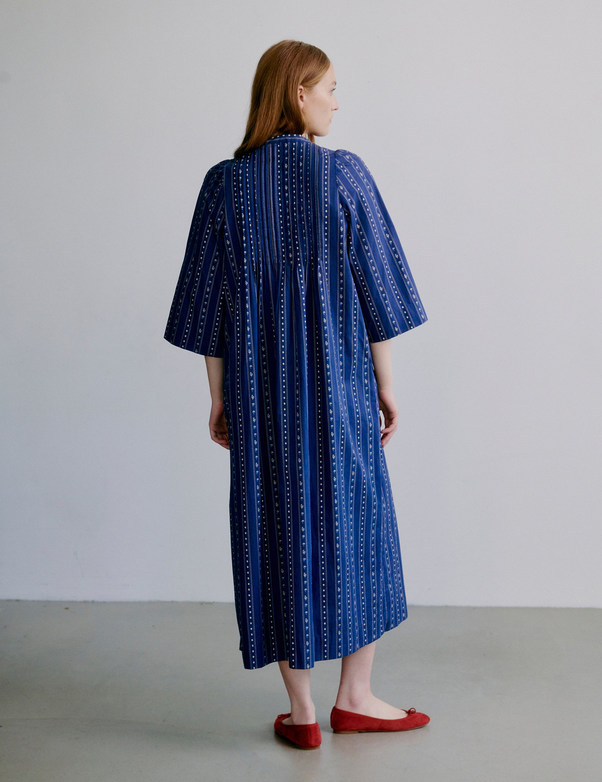 Woman wearing a blue stripe patterned dress with buttons and semi-long wide sleeves