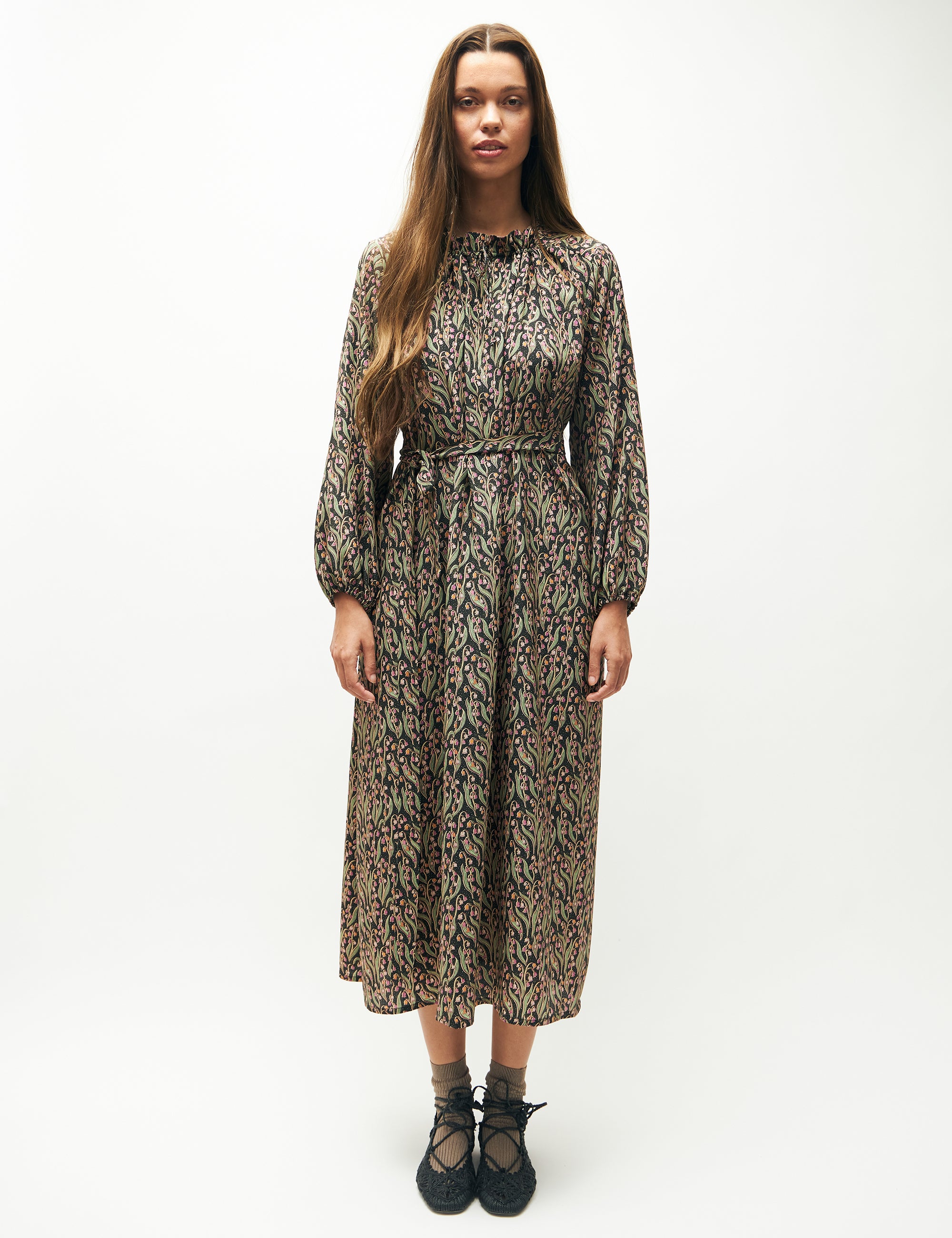 Woman in long sleeved dress with pink and green flower pattern and matching belt