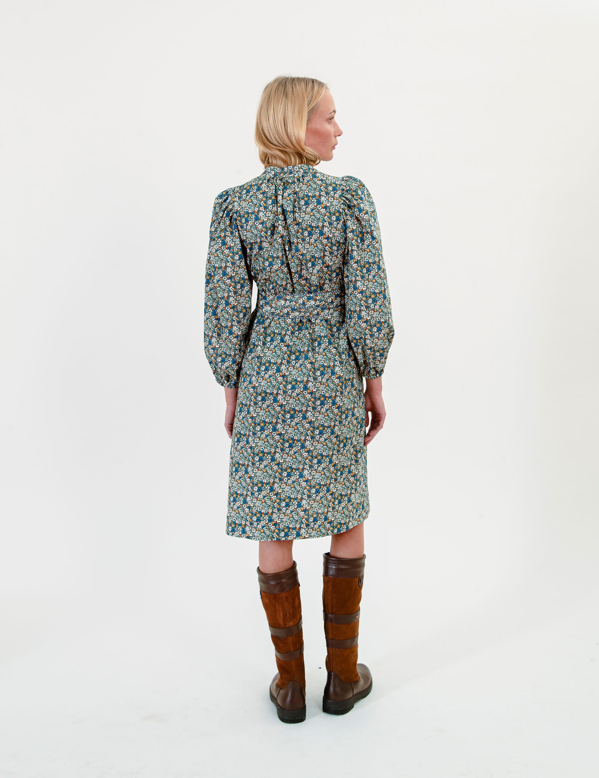 Woman wearing a short green-blue floral dress with long sleeves and a belt on a white background