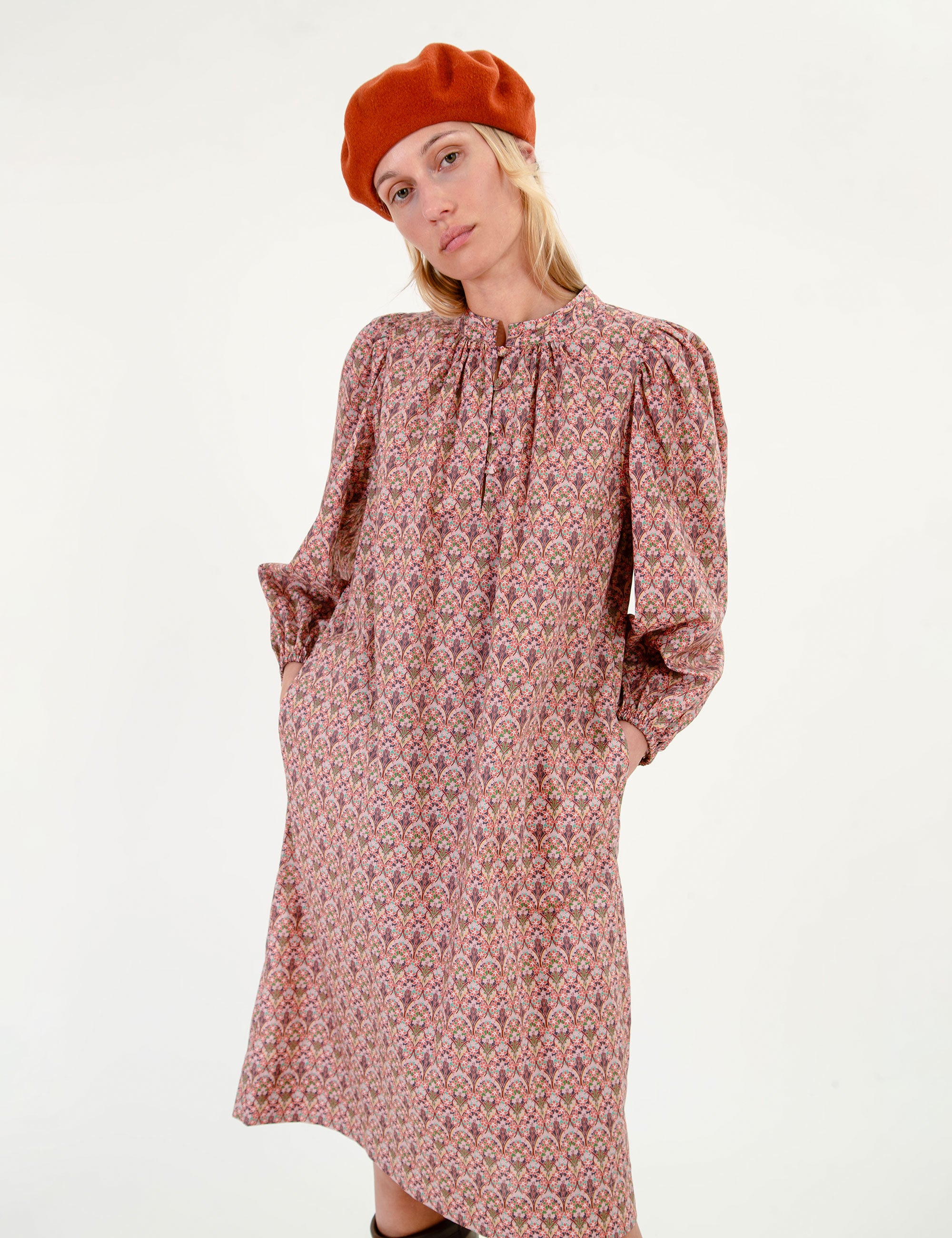 Woman wearing a floral patterned dress with long sleeves and a fabric belt, brown boots, and a red beret on a white background