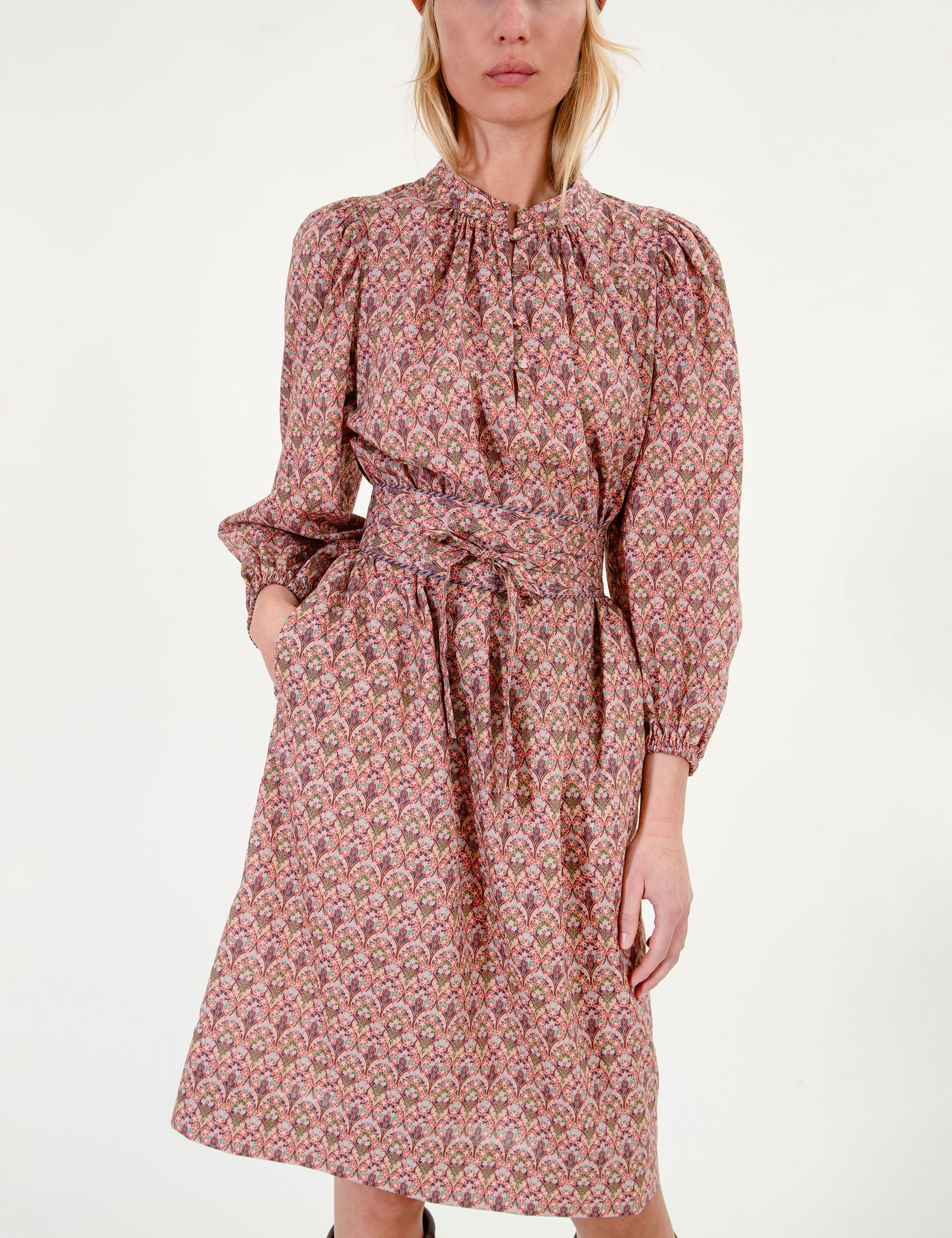 Woman wearing a floral patterned dress with long sleeves and a fabric belt, brown boots, and a red beret on a white background