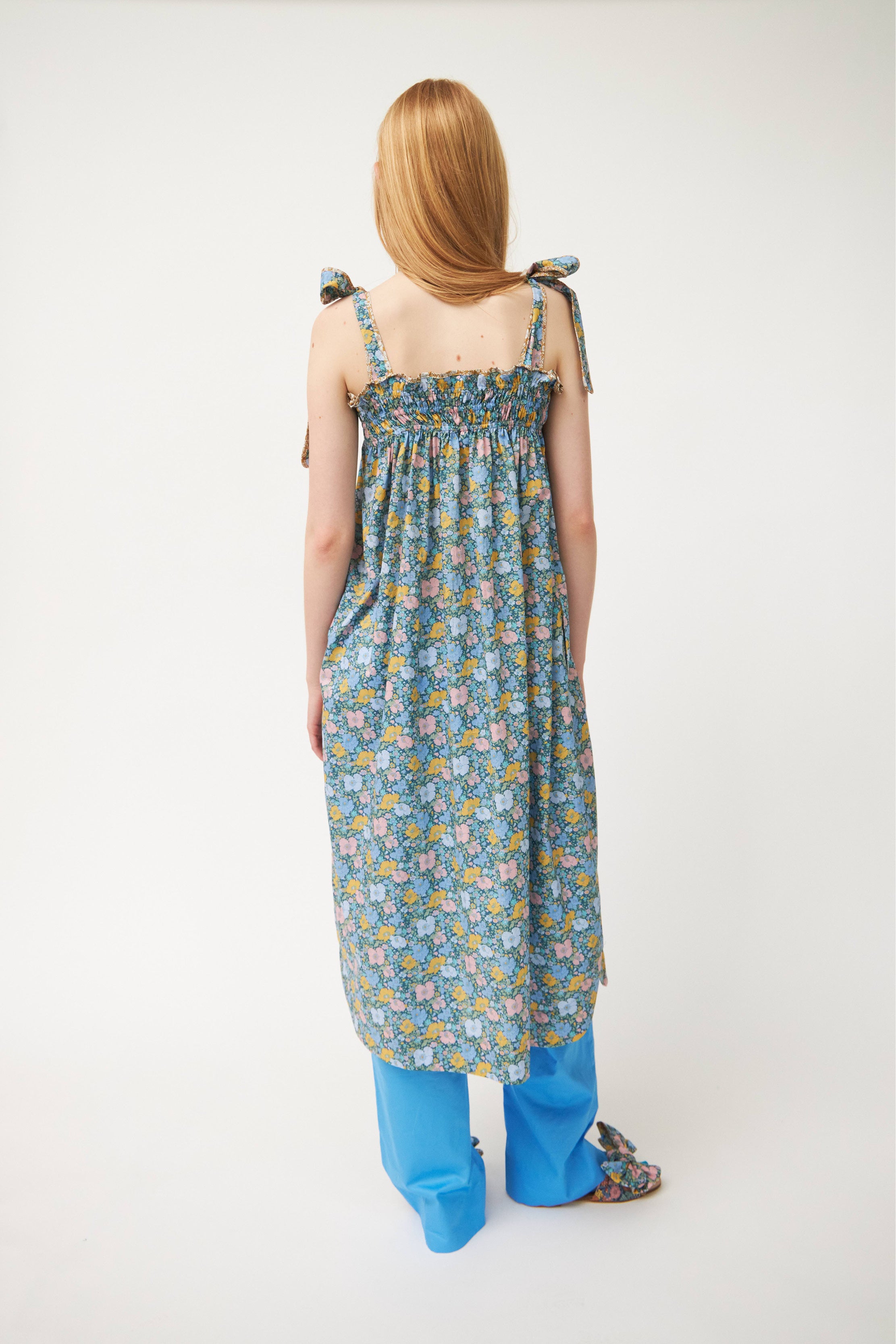 Woman in blue cotton pants, strap dress with multi-colored floral print and sandals with floral print bows