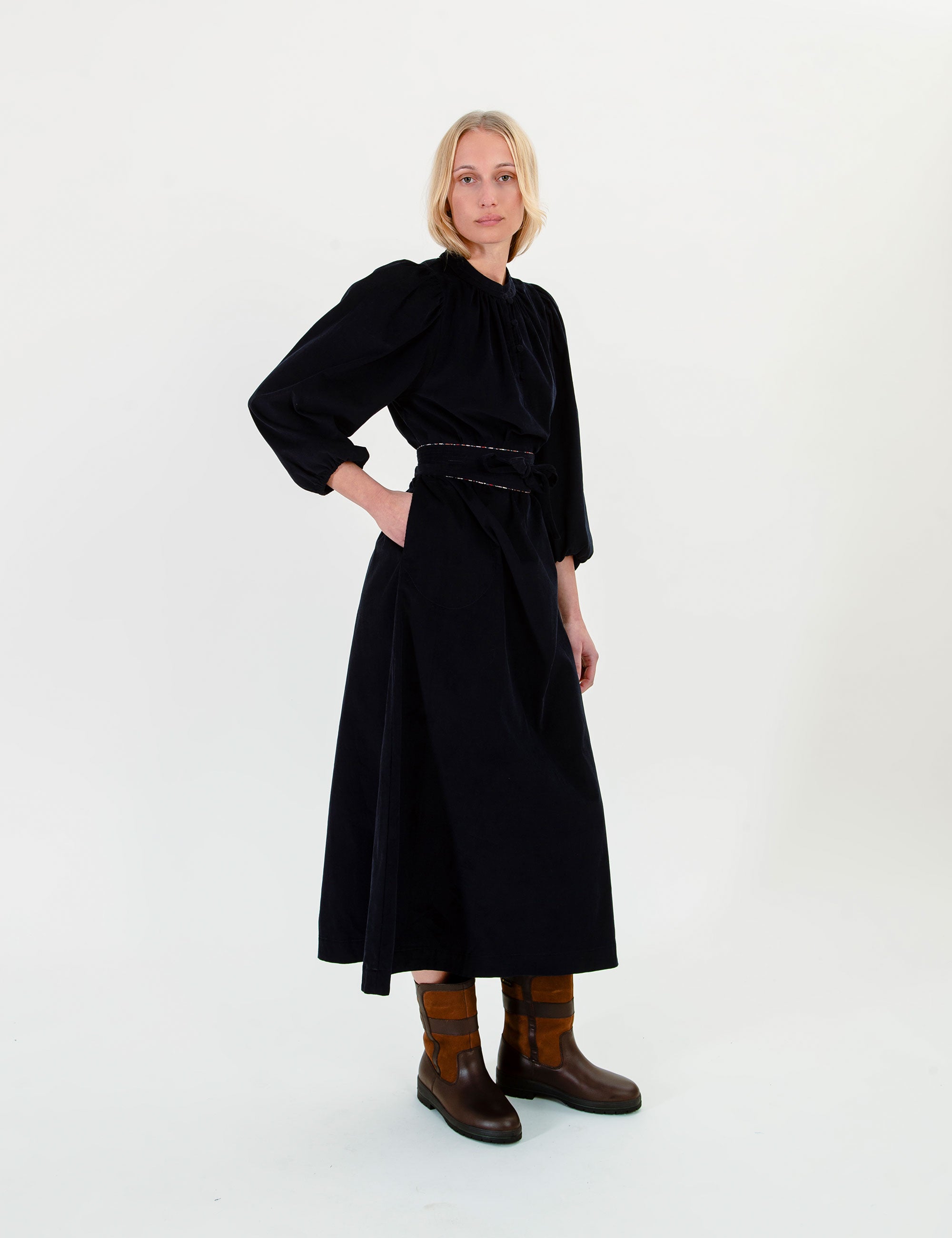 Woman wearing a dark blue corduroy  dress with long puff sleeves a belt on a white backgroundnd 