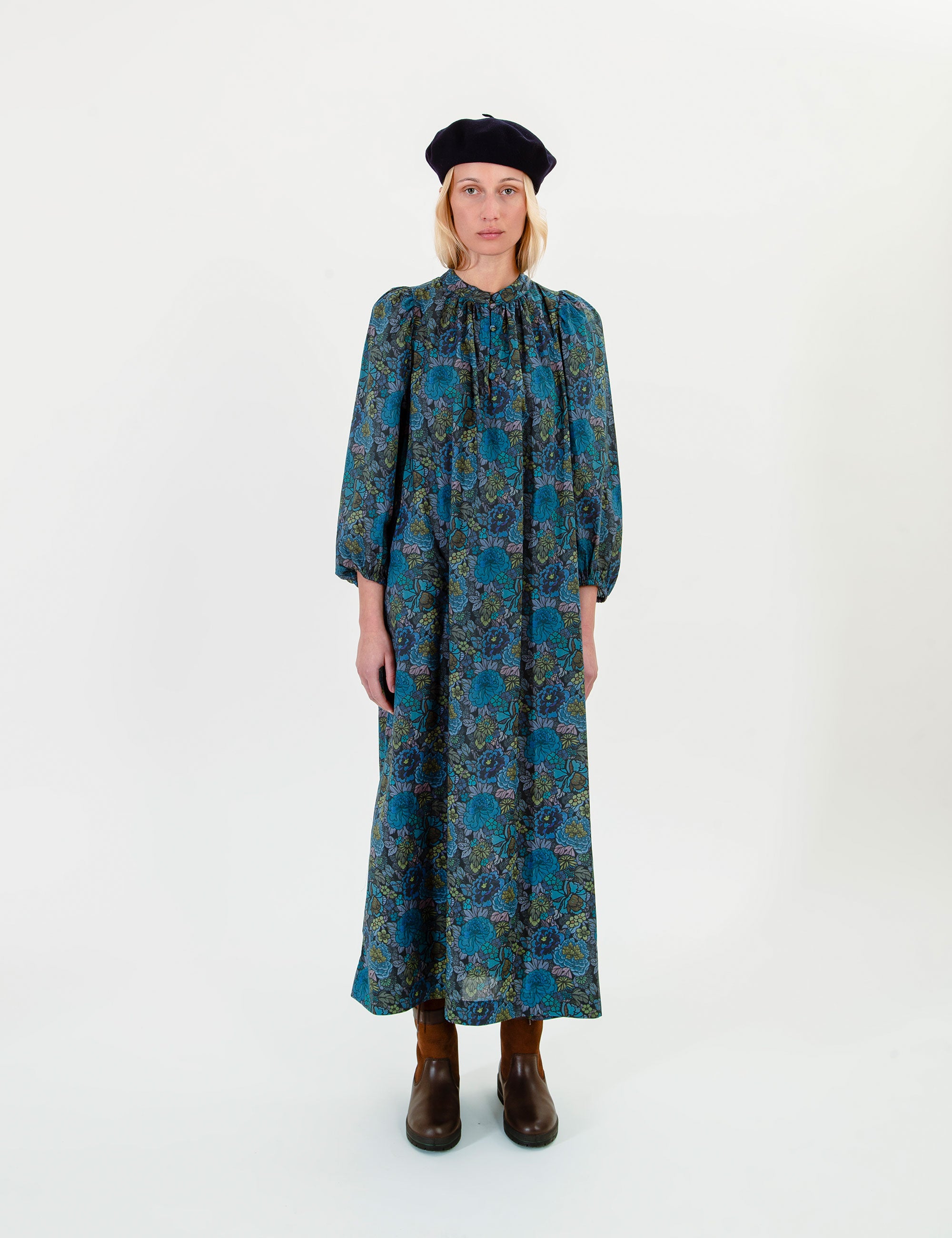 Woman wearing a long blue-green floral dress with a white background