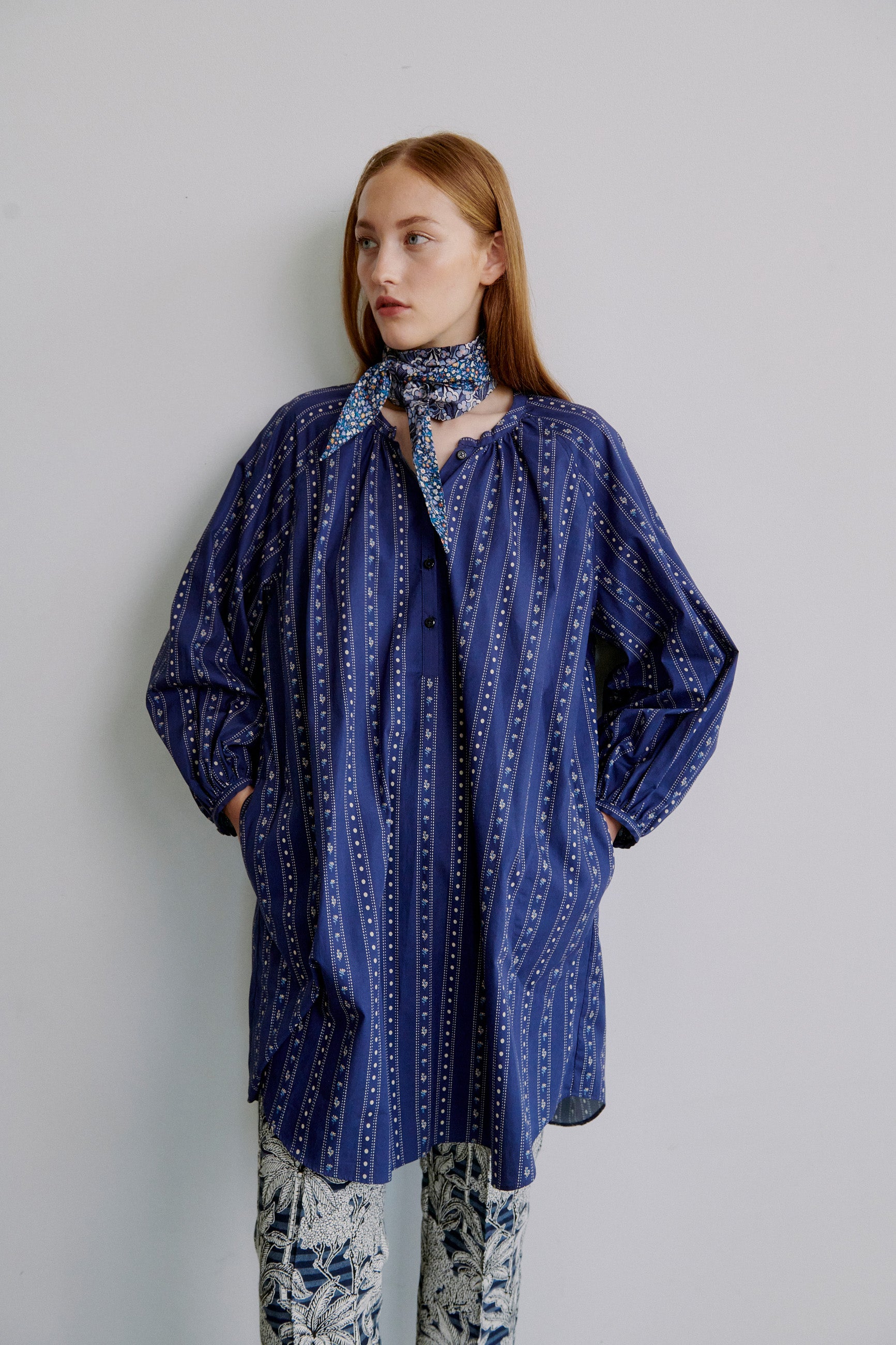 Woman wearing a blue patterned long shirt  with long sleeves, blue floral patterned pants and a blue floral scarf around neck