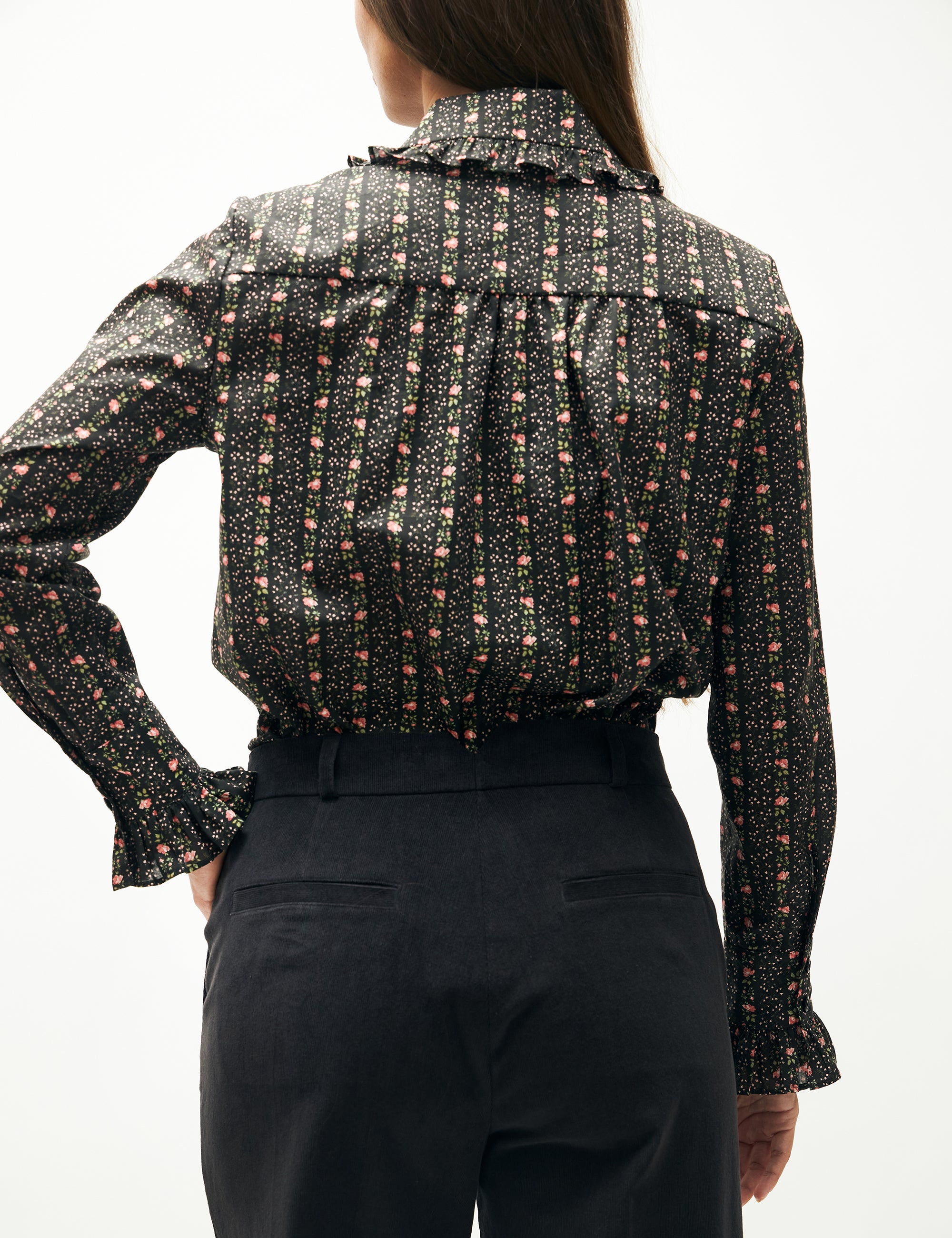 Woman in blue corduroy pants and long sleeved shirt with flower pattern and frills
