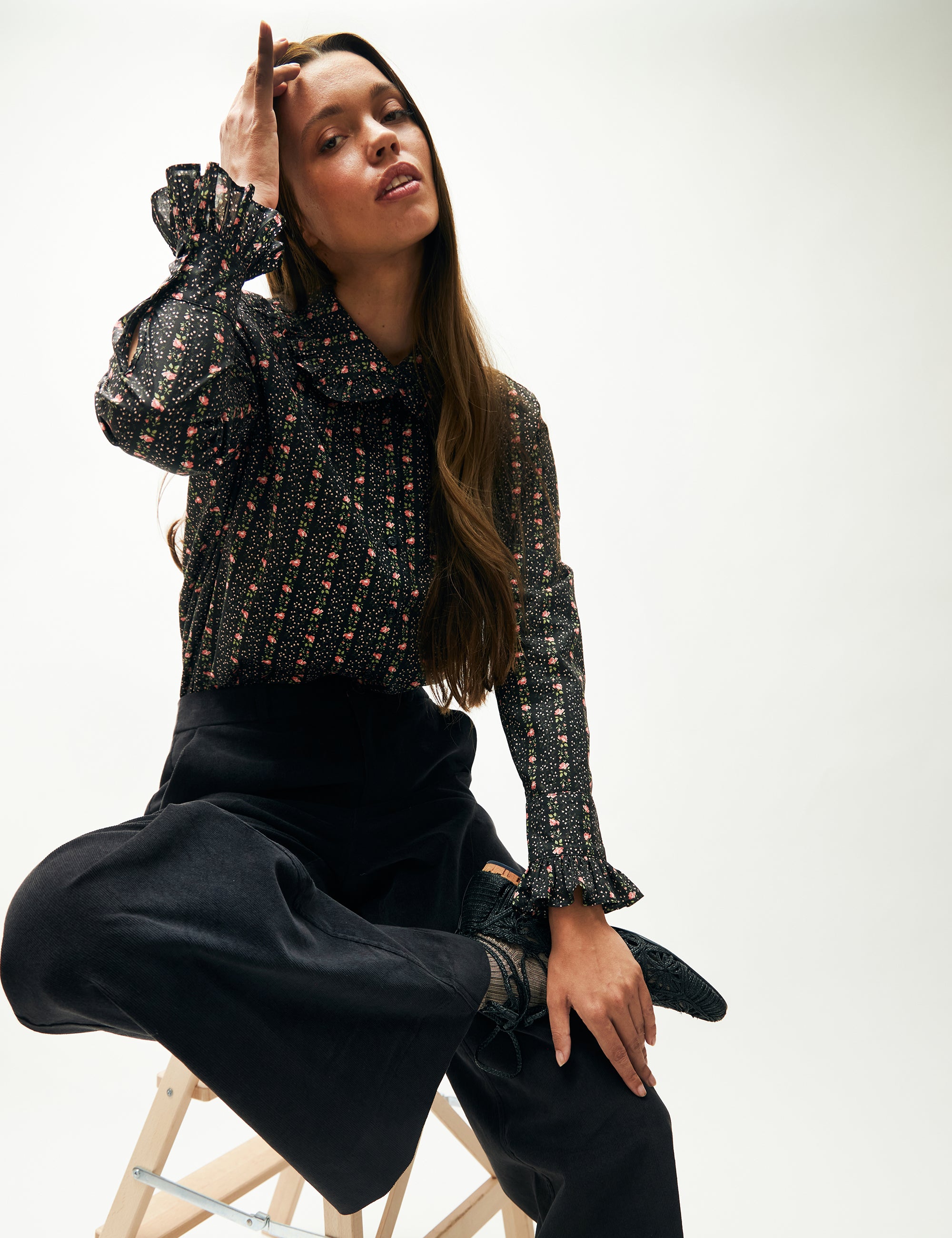 Woman in blue corduroy pants and long sleeved shirt with flower pattern and frills