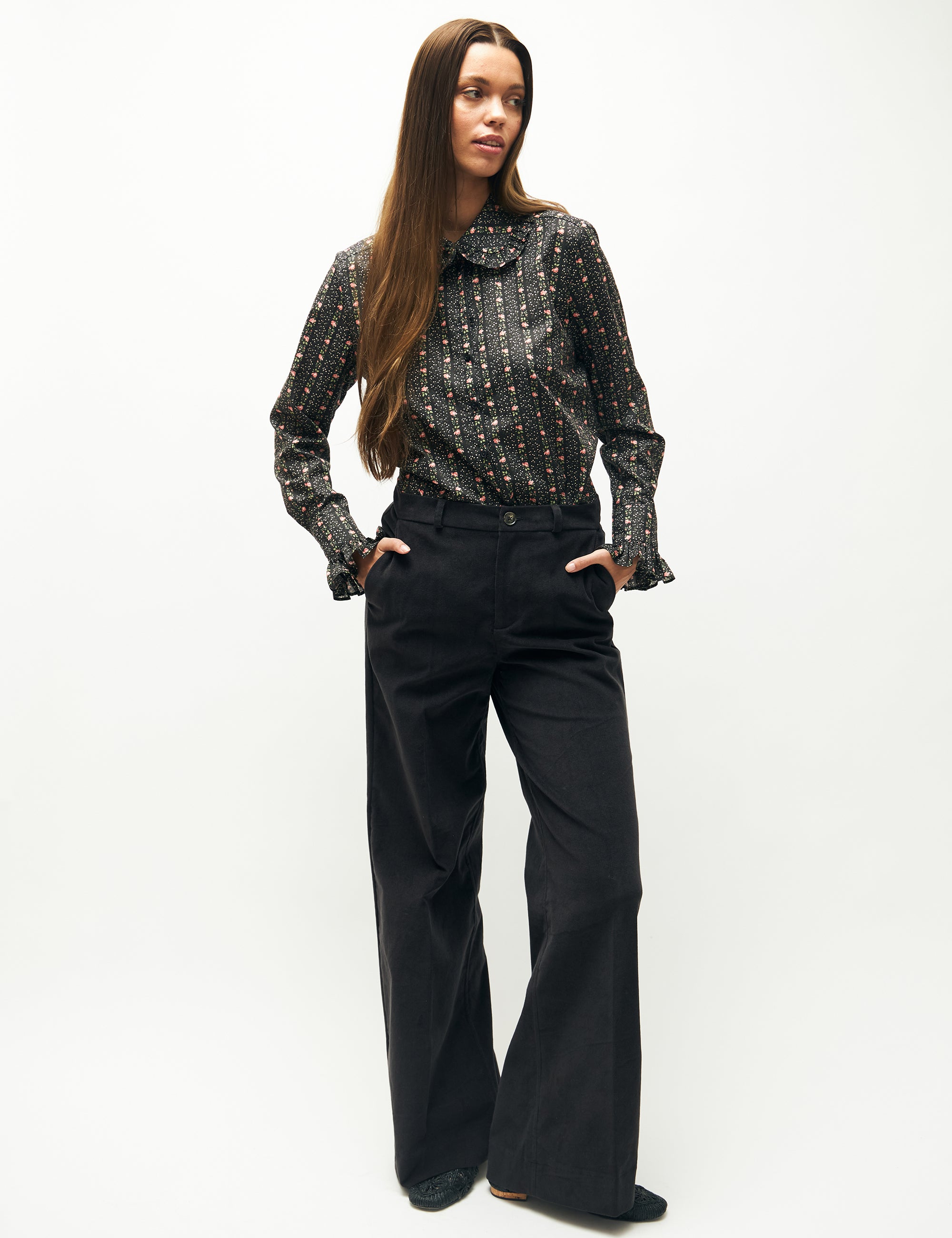 Woman in blue corduroy pants and long sleeved shirt with flower pattern and frills