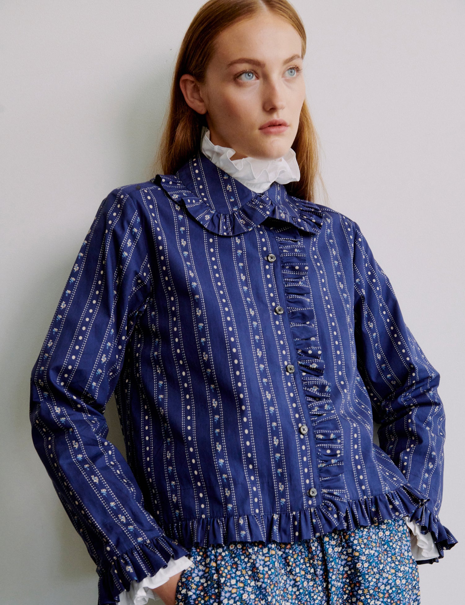 Woman wearing a blue patterned jacket with frills and buttons with a white collar and floral patterned pants