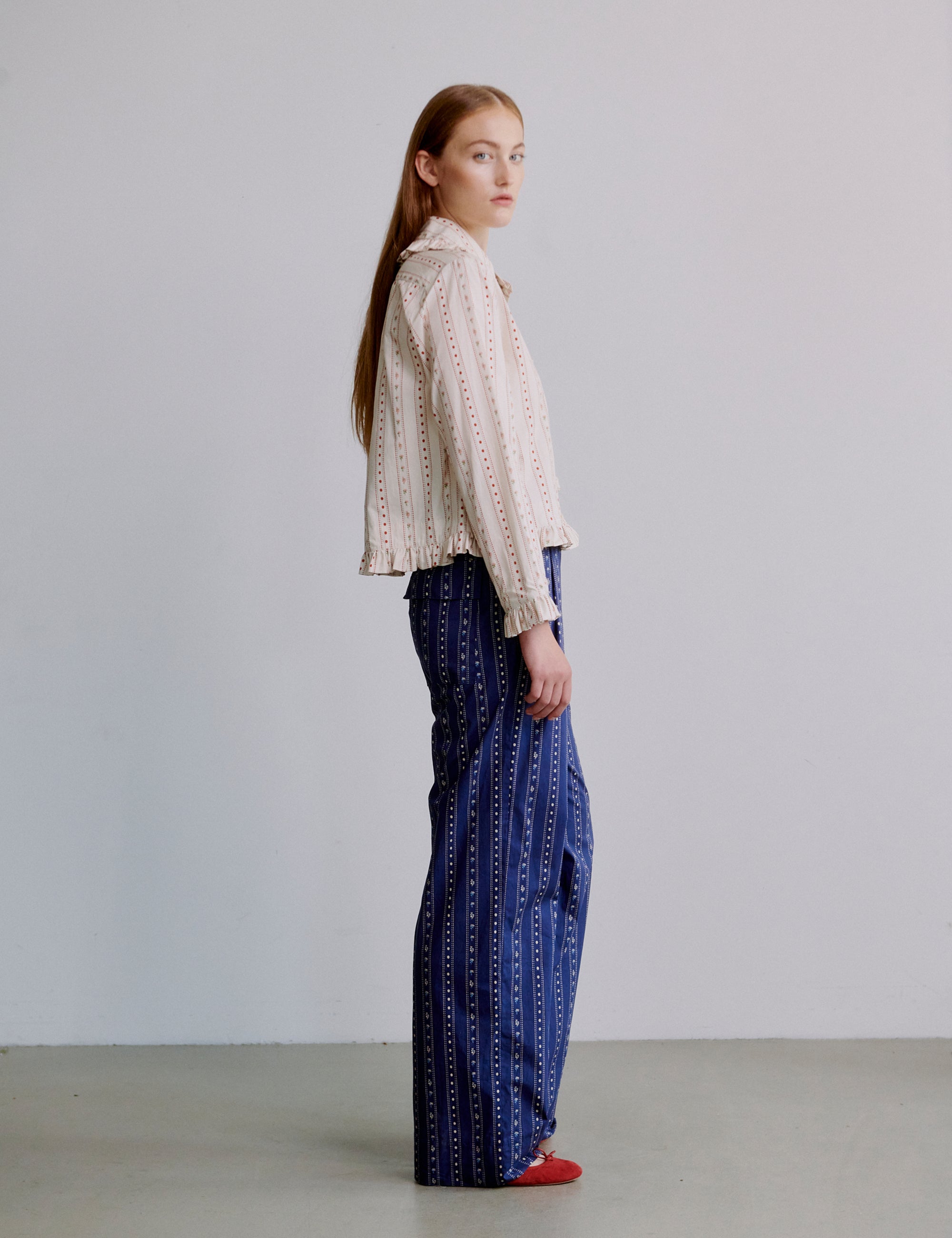 Woman wearing a white and pink floral patterned blouse and blue patterned pants against a plain background