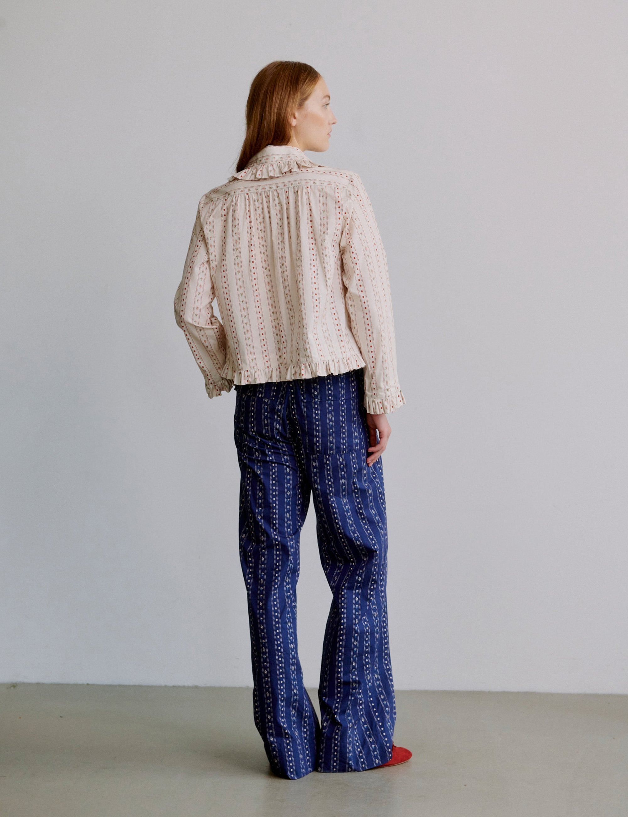 Woman wearing a white and pink floral patterned blouse and blue patterned pants against a plain background