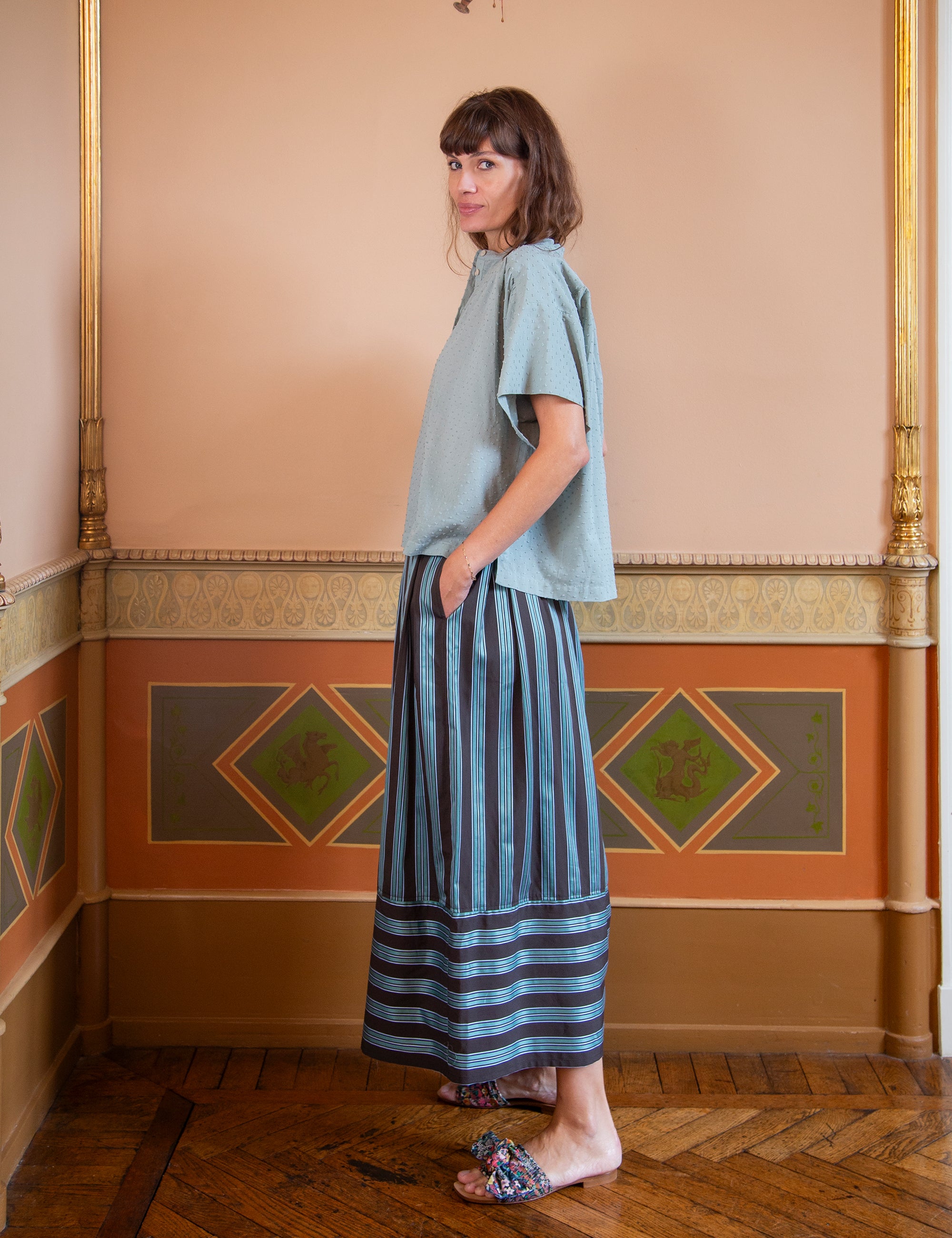 Woman wearing a light green top and striped skirt standing in a room with decorative walls.