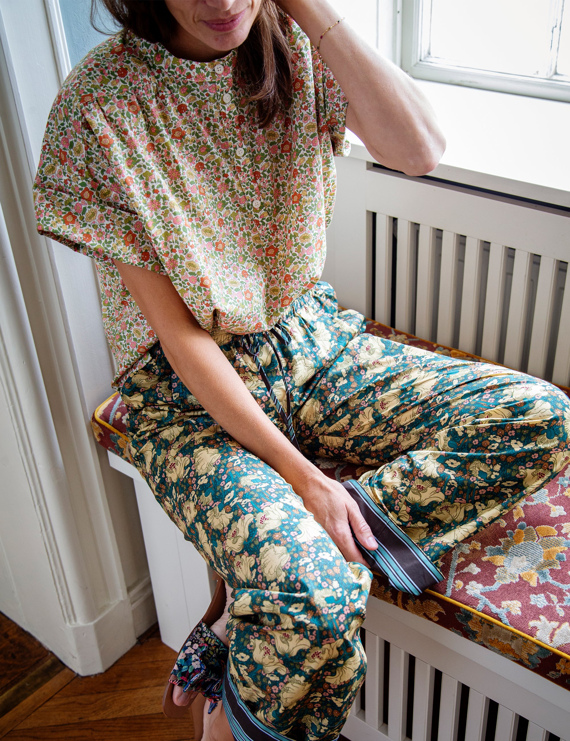Woman wearing a floral patterned top and green floral pants sitting on a bench