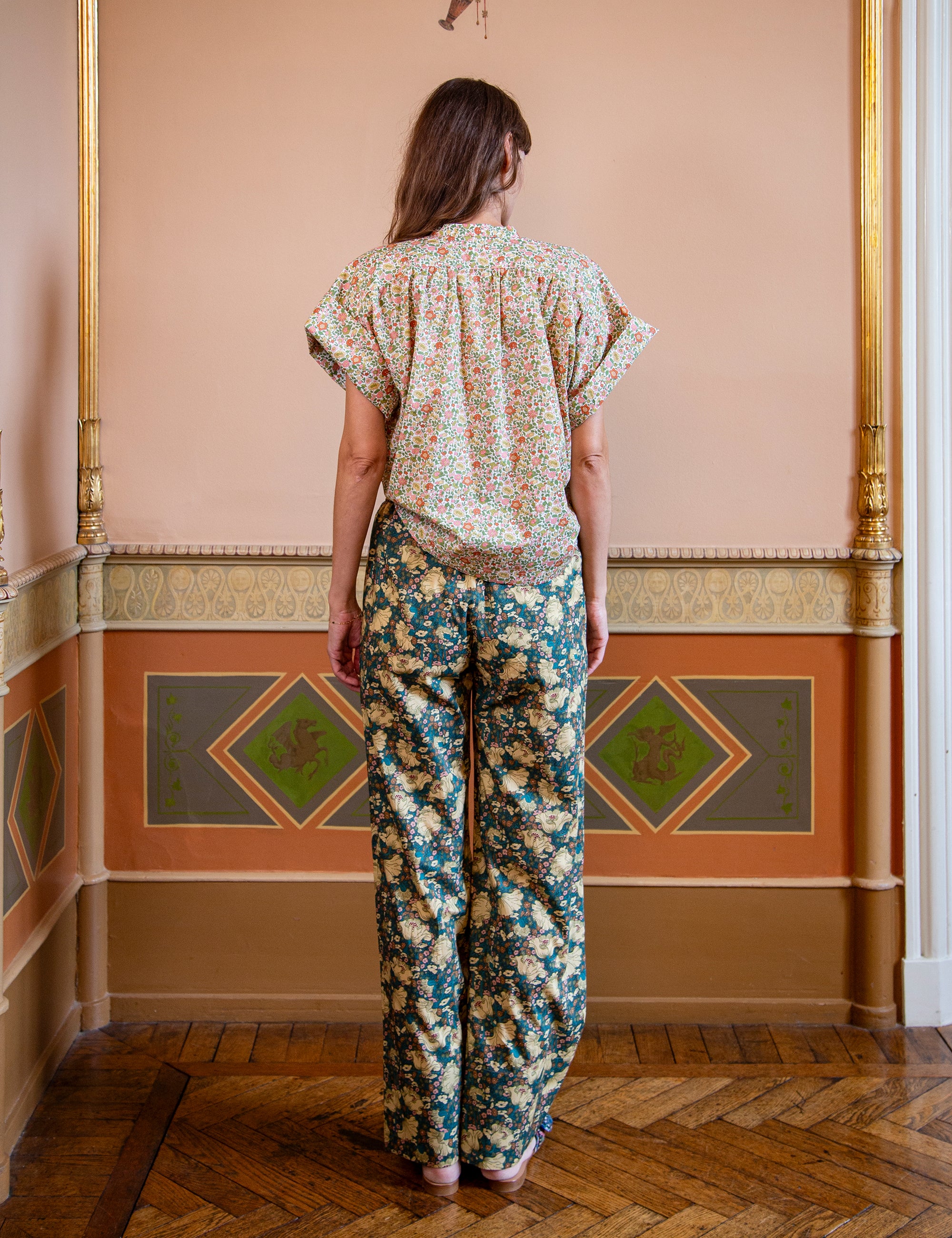 Woman wearing a floral patterned top and green floral pants in an ornate room.