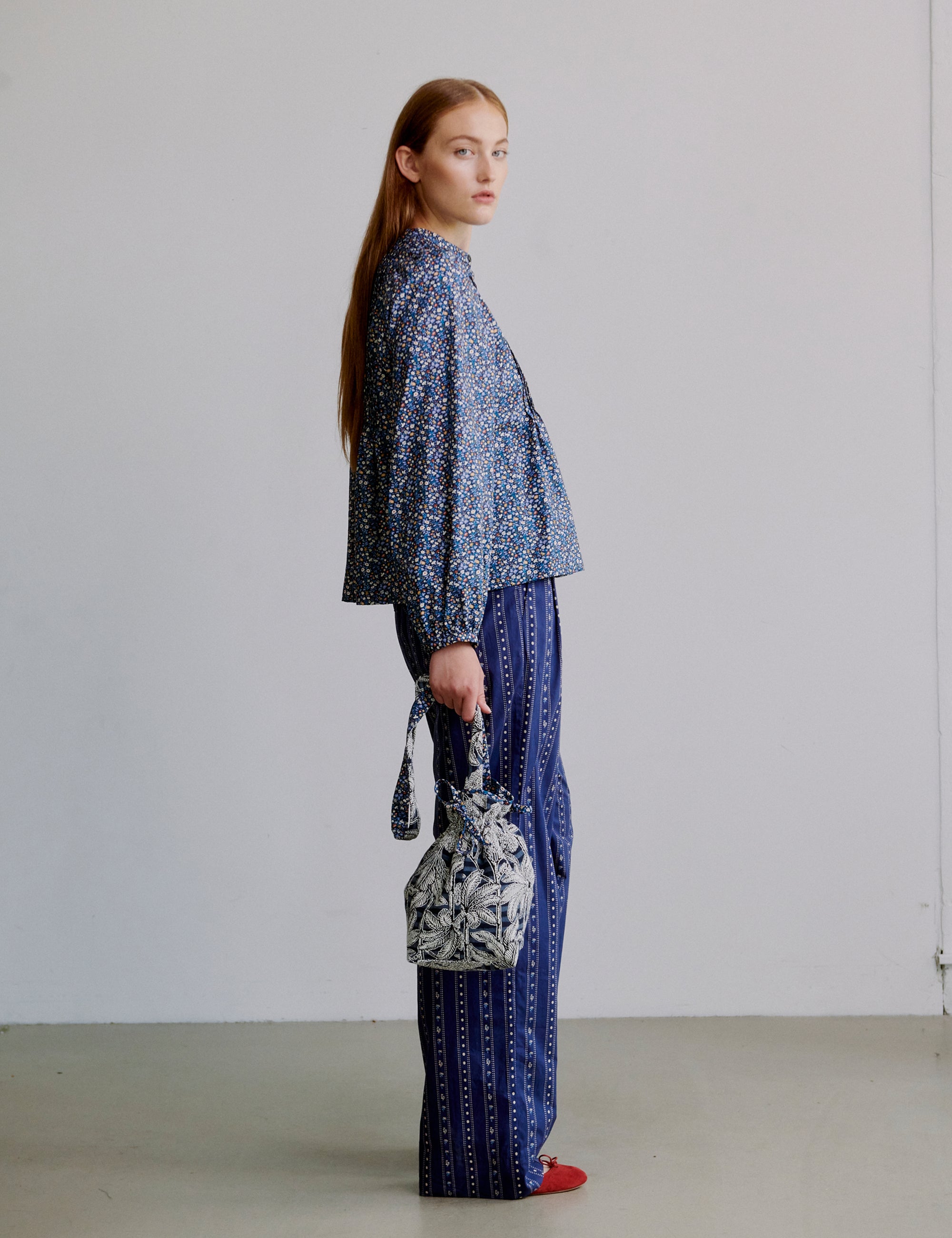 Woman wearing a blue floral patterned long sleeve shirt and blue striped pants holding a blue floral bag