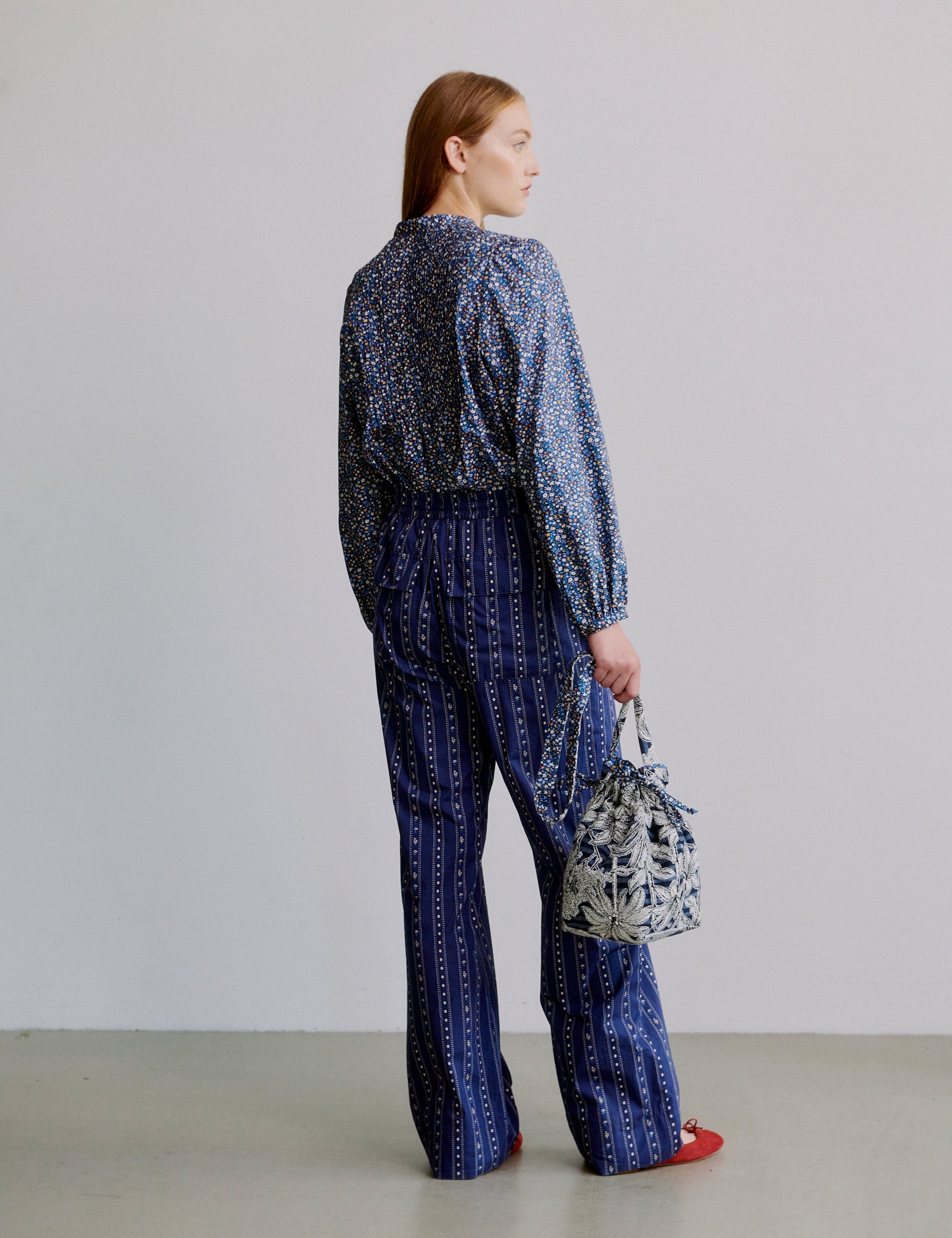 Woman wearing a blue floral patterned long sleeve shirt and blue striped pants holding a blue floral bag