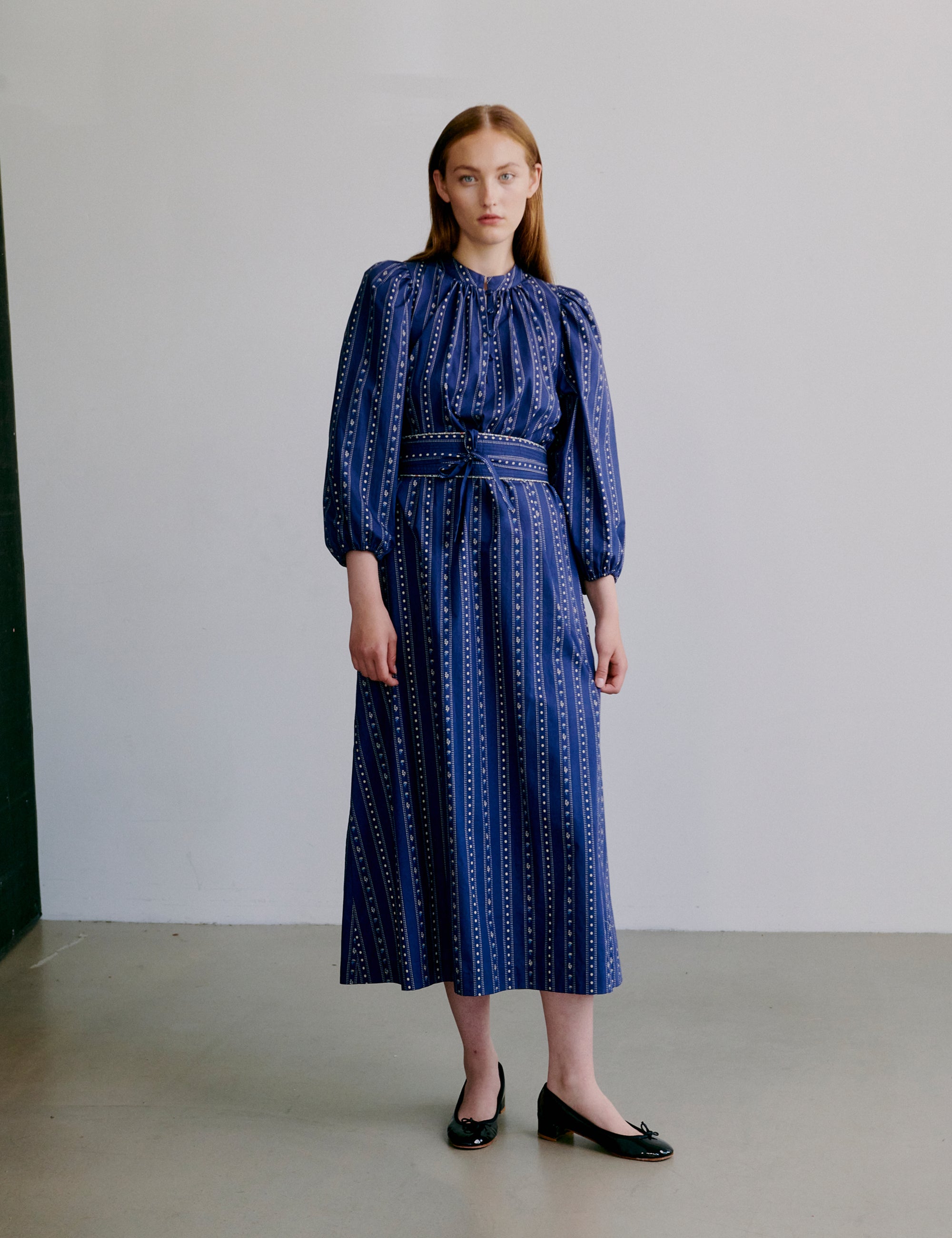 Woman wearing a blue patterned dress with long puff sleeves, collar buttons and matching belt