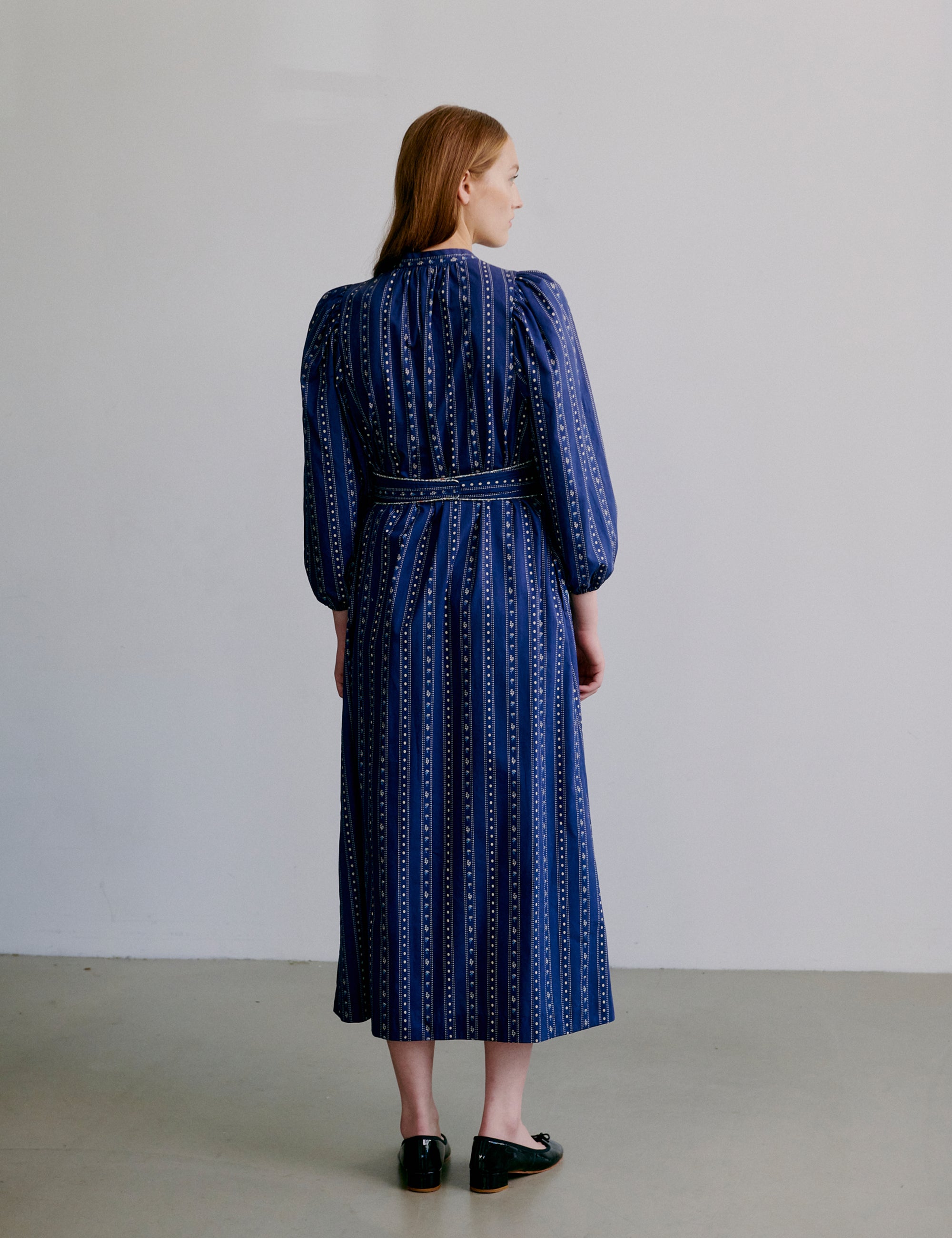 Woman wearing a blue patterned dress with long puff sleeves, collar buttons and matching belt